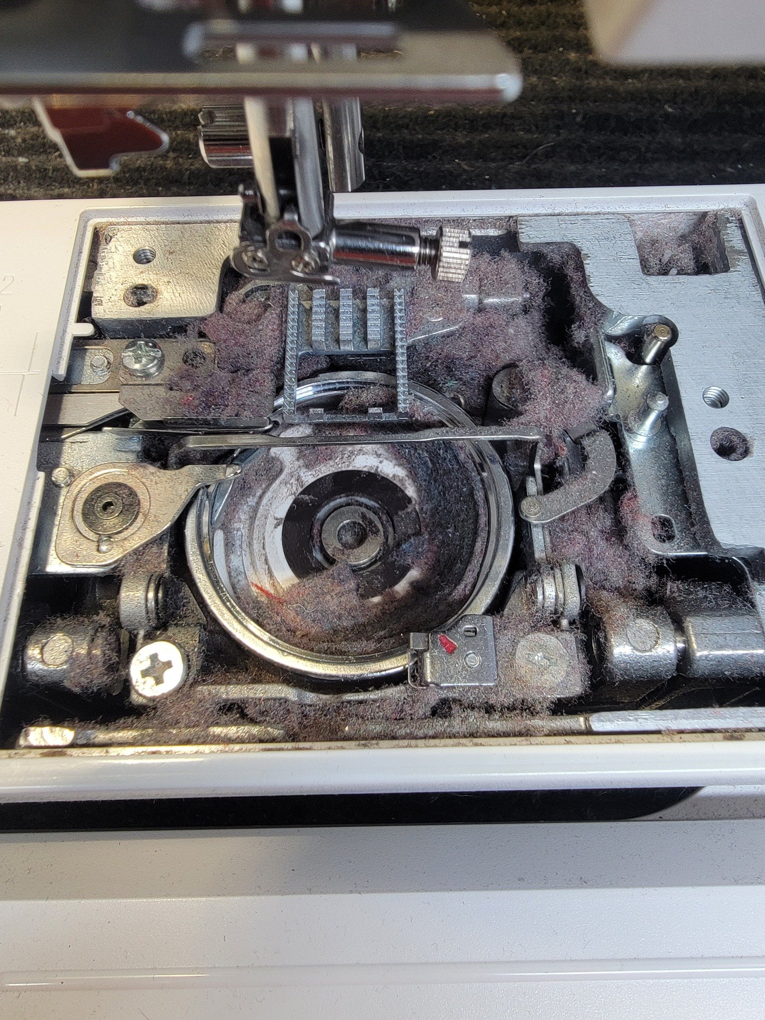 Close-up view of the inner mechanical components of a sewing machine, showing gears, a metal rod, and dust. The outer casing is removed, exposing the internal machinery.