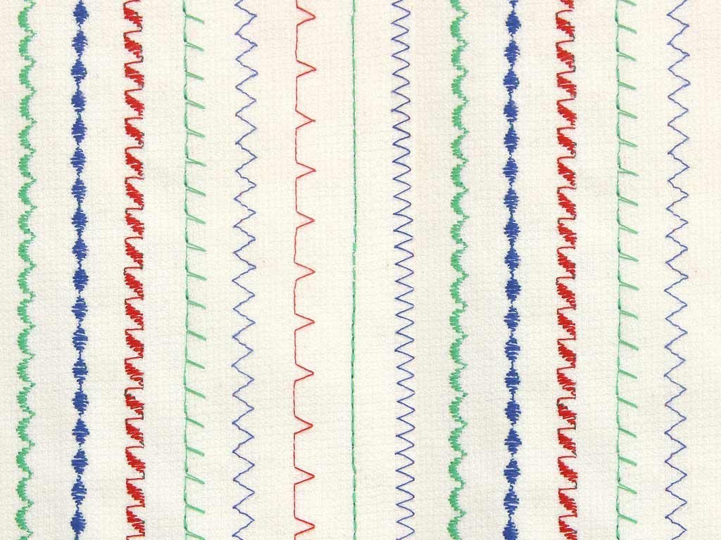 Close-up of sewing machine stitches with alternating vertical rows in red, green, blue, and purple thread.