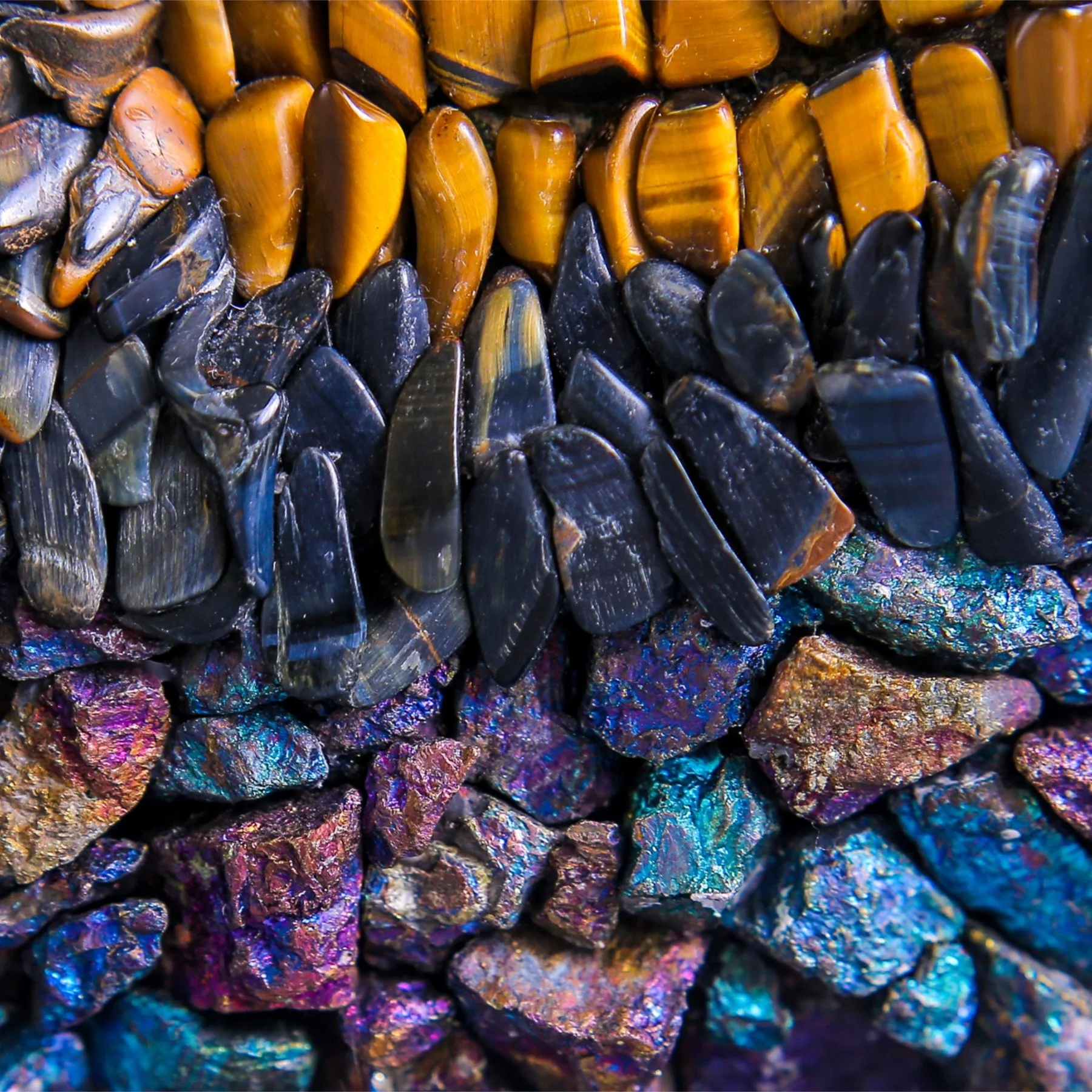Close-up of various colorful iridescent stones or minerals with shiny, reflective surfaces and vibrant hues.