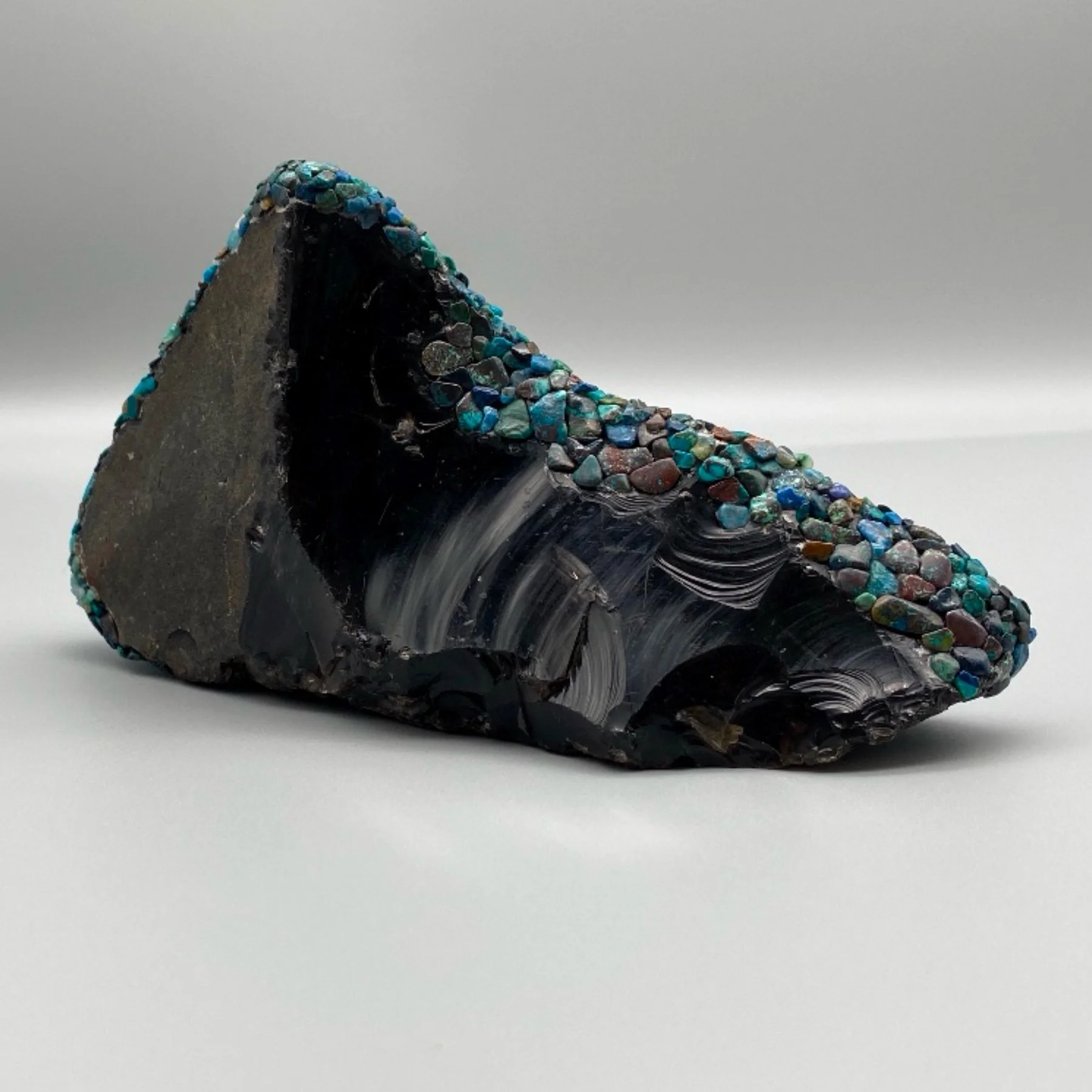 Close-up of a material with black and gray swirled pattern decorated with small, colorful, polished gemstones along the top edge.