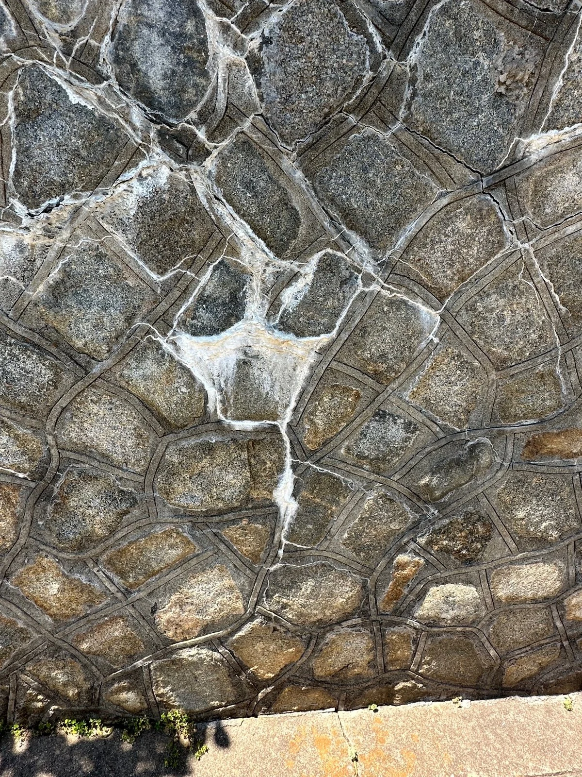 Close-up of a stone wall with irregularly shaped stones held together with white mortar, showing cracks and natural textures.