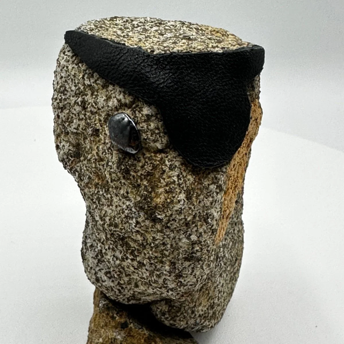 A piece of rock with a black leather cap and a shiny black stone attached, resembling a face.