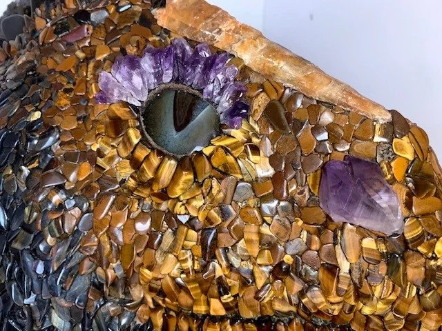 Close-up of a dragon sculpture made from various small gemstone chips, featuring a large eye with purple and brown gemstone accents.