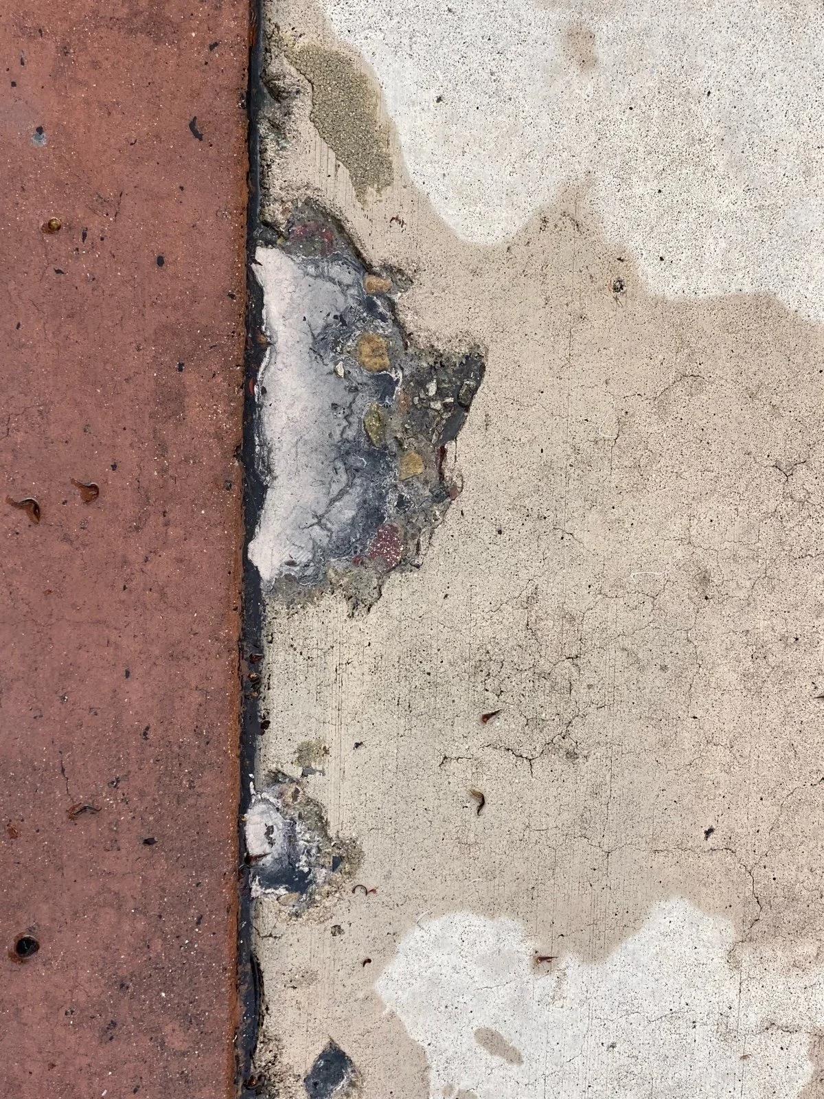 A concrete sidewalk with a large chipped area exposing the underlying materials, next to a red brick surface.