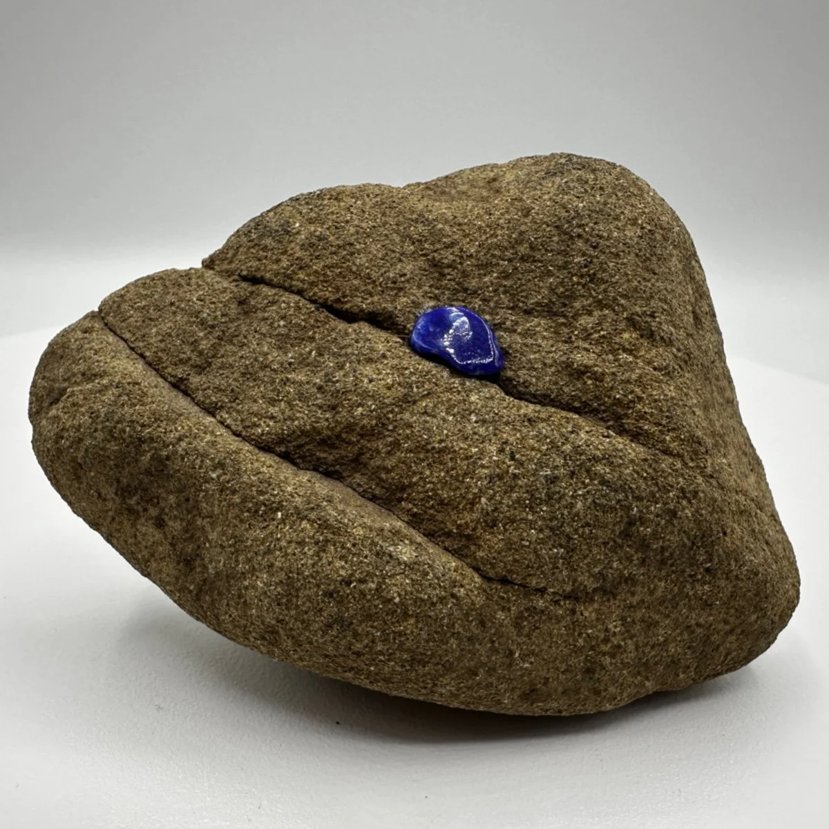 A smooth, rounded brown rock with a small, shiny blue gemstone on top.