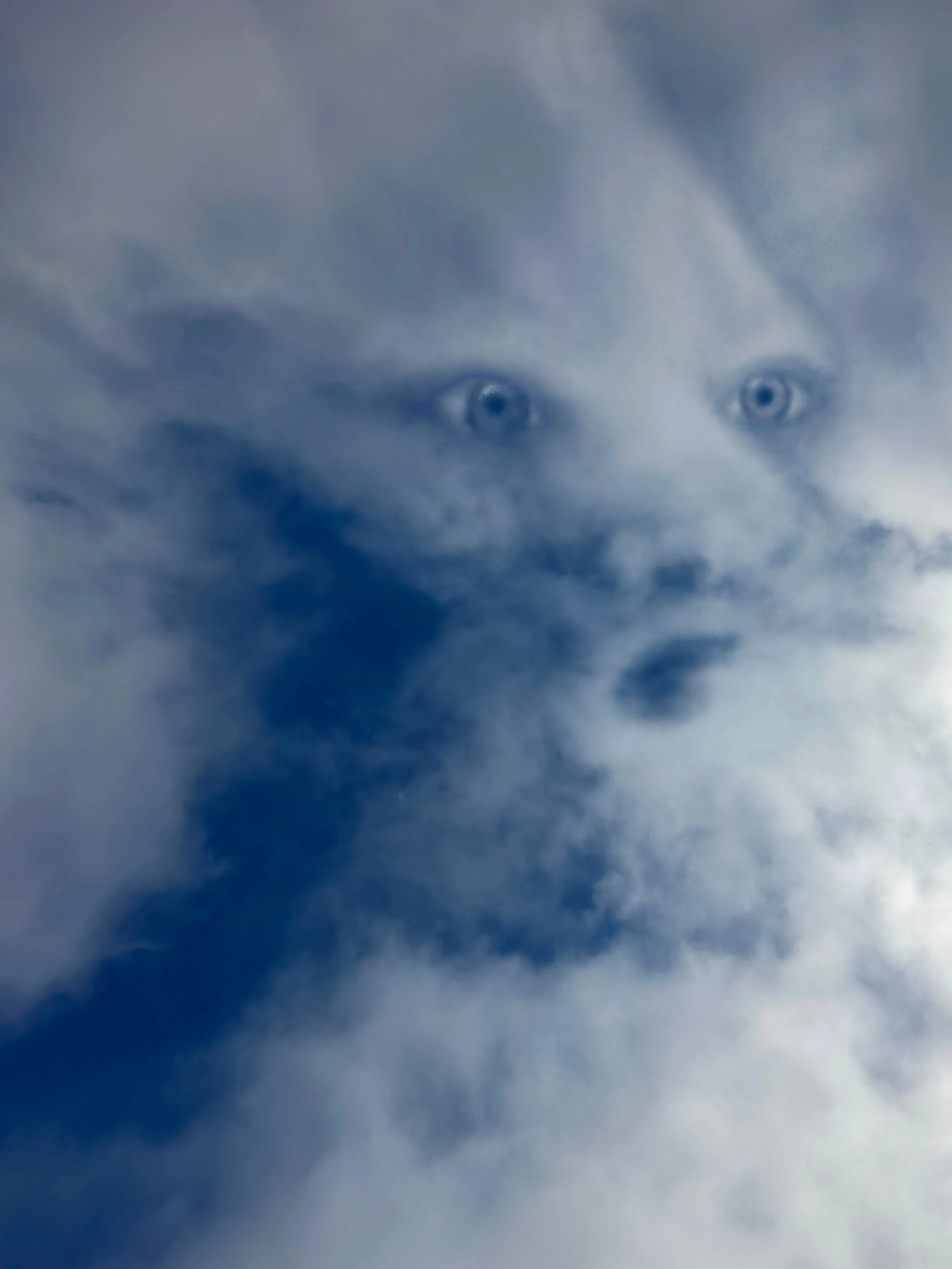 A cloudy sky with a person's face appearing through the clouds, showing eyes and part of the nose.