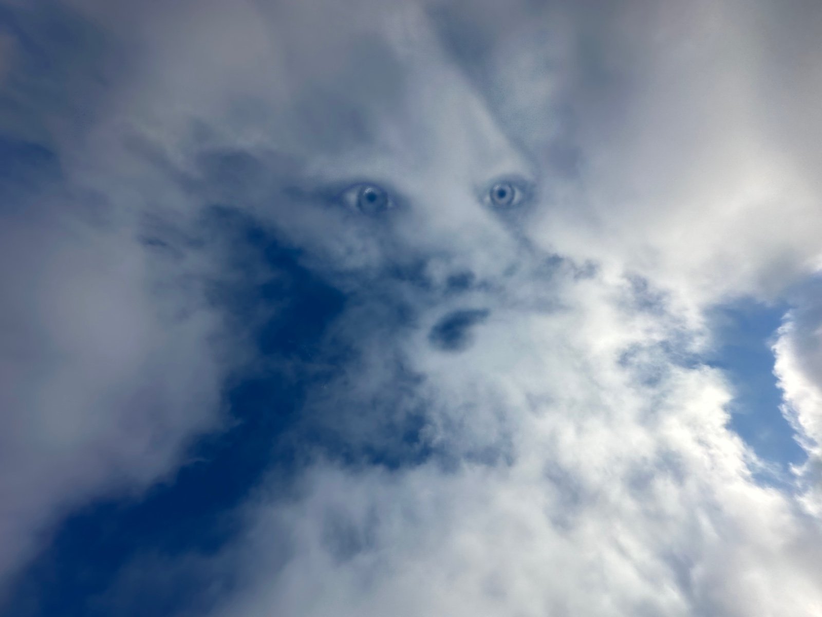 A sky with clouds and a faint face of a person with blue eyes visible through the clouds.