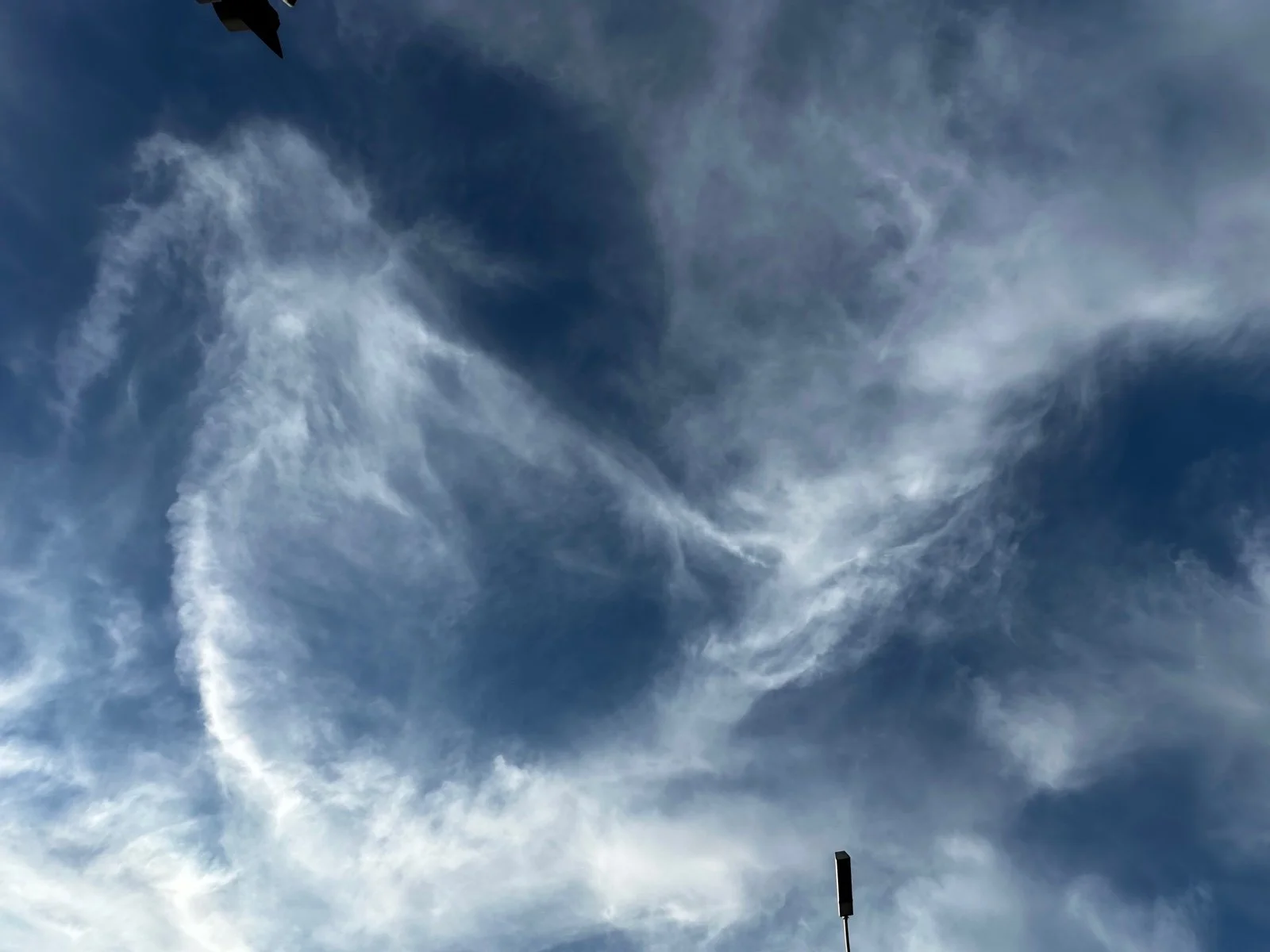 Blue sky with white, wispy clouds and a black flagpole at the bottom.