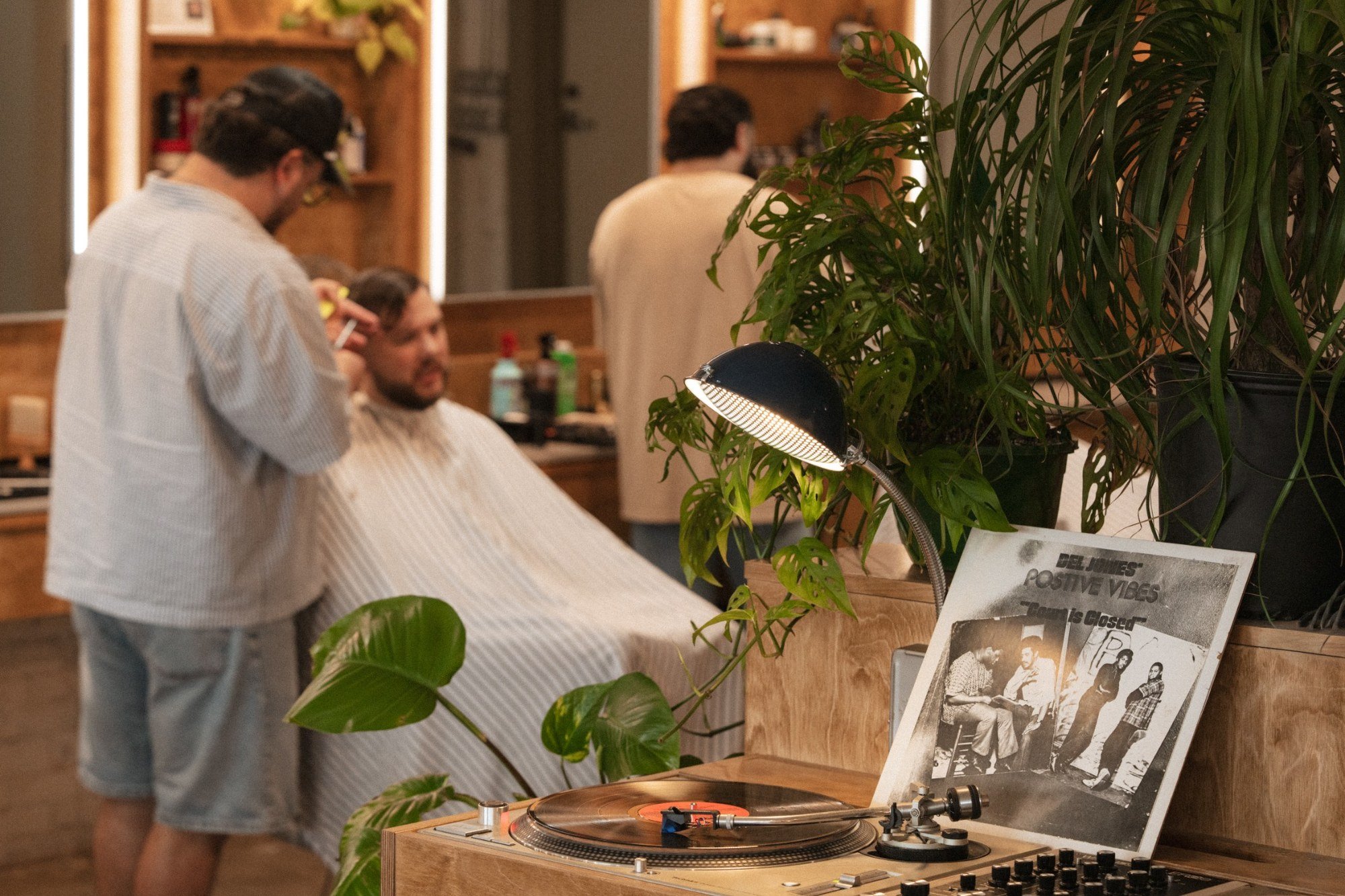 Barber providing a haircut beside a turntable and houseplants inside Fort Worth Barbershop in Near Southside Fort Worth.