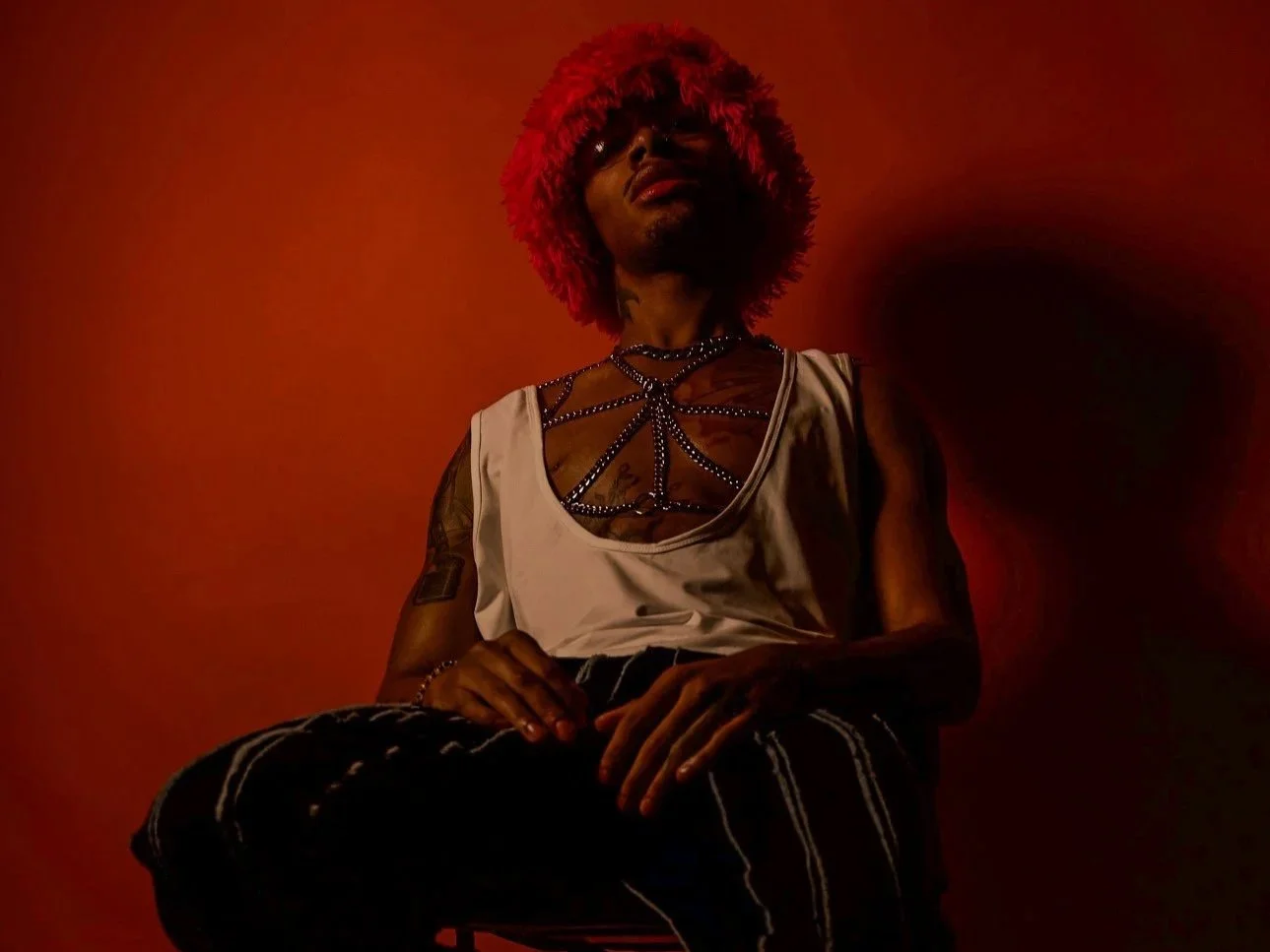 Person with red hat wearing a white sleeveless top with rhinestone design, sitting against a red background with shadow. Modeling inspiration