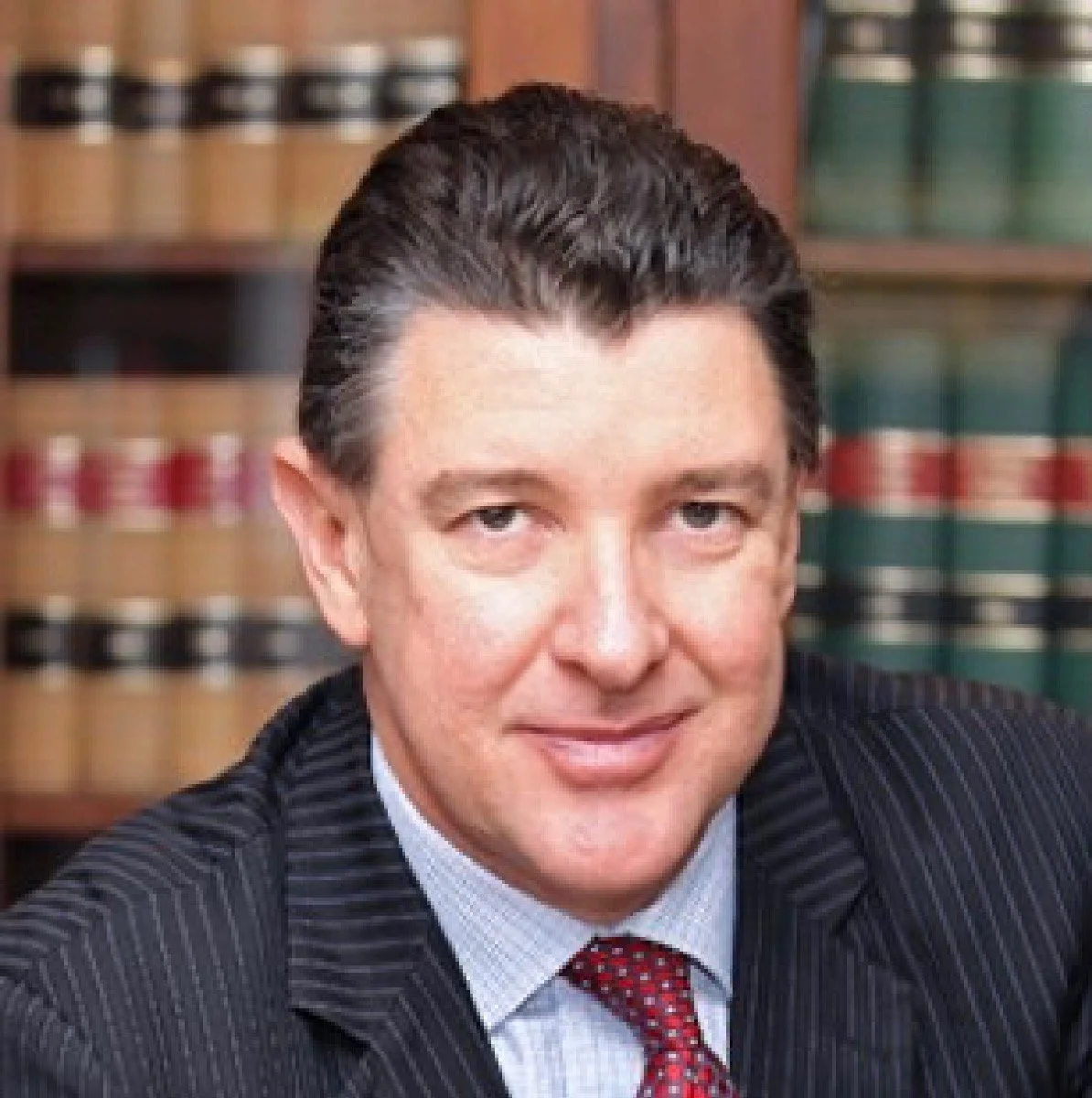 Portrait of Keith Howe in a legal office, wearing a suit and tie, with legal books on shelves in the background.