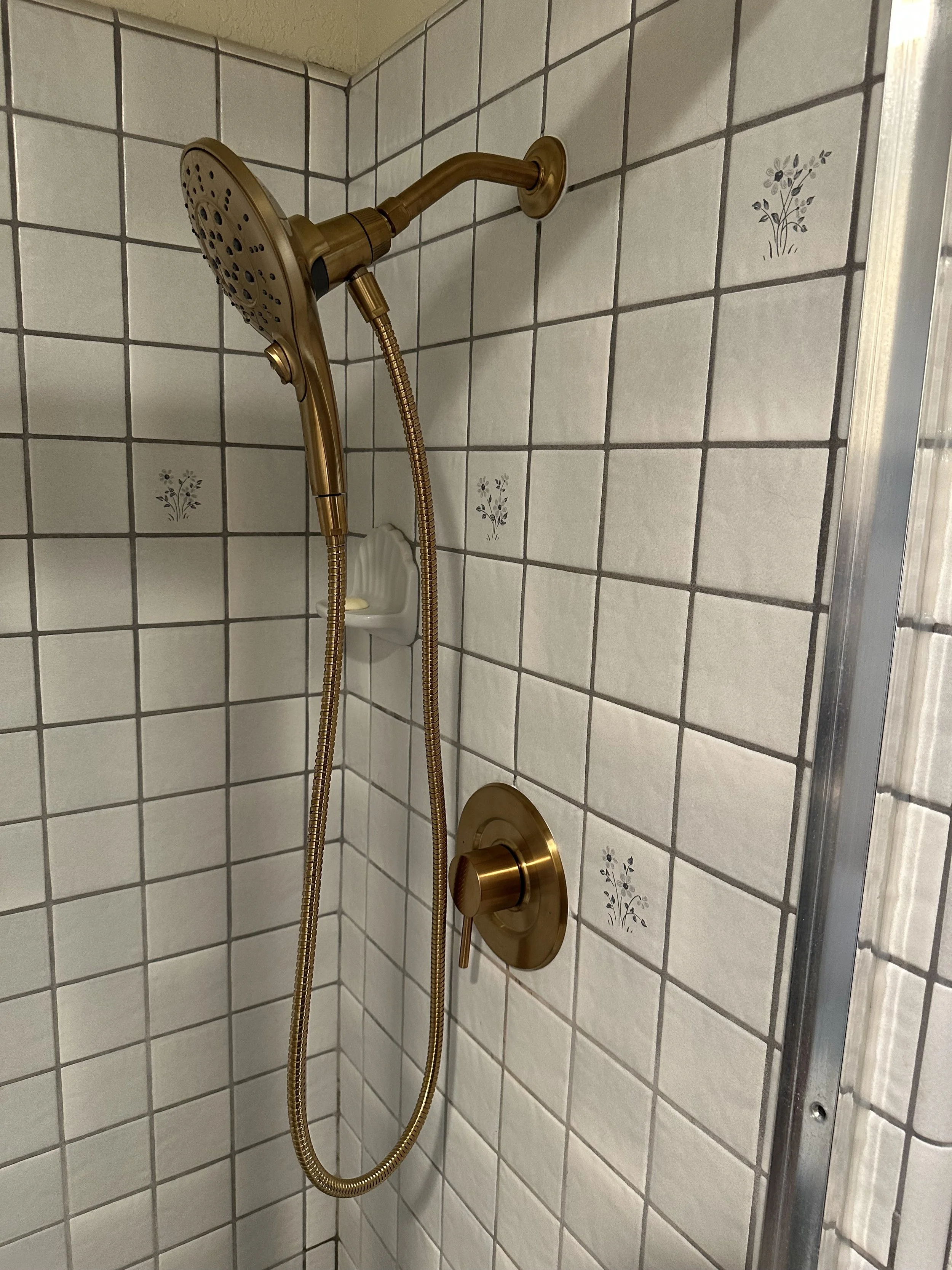 Bronze-colored shower head attached to a tiled wall with floral decorated tiles.