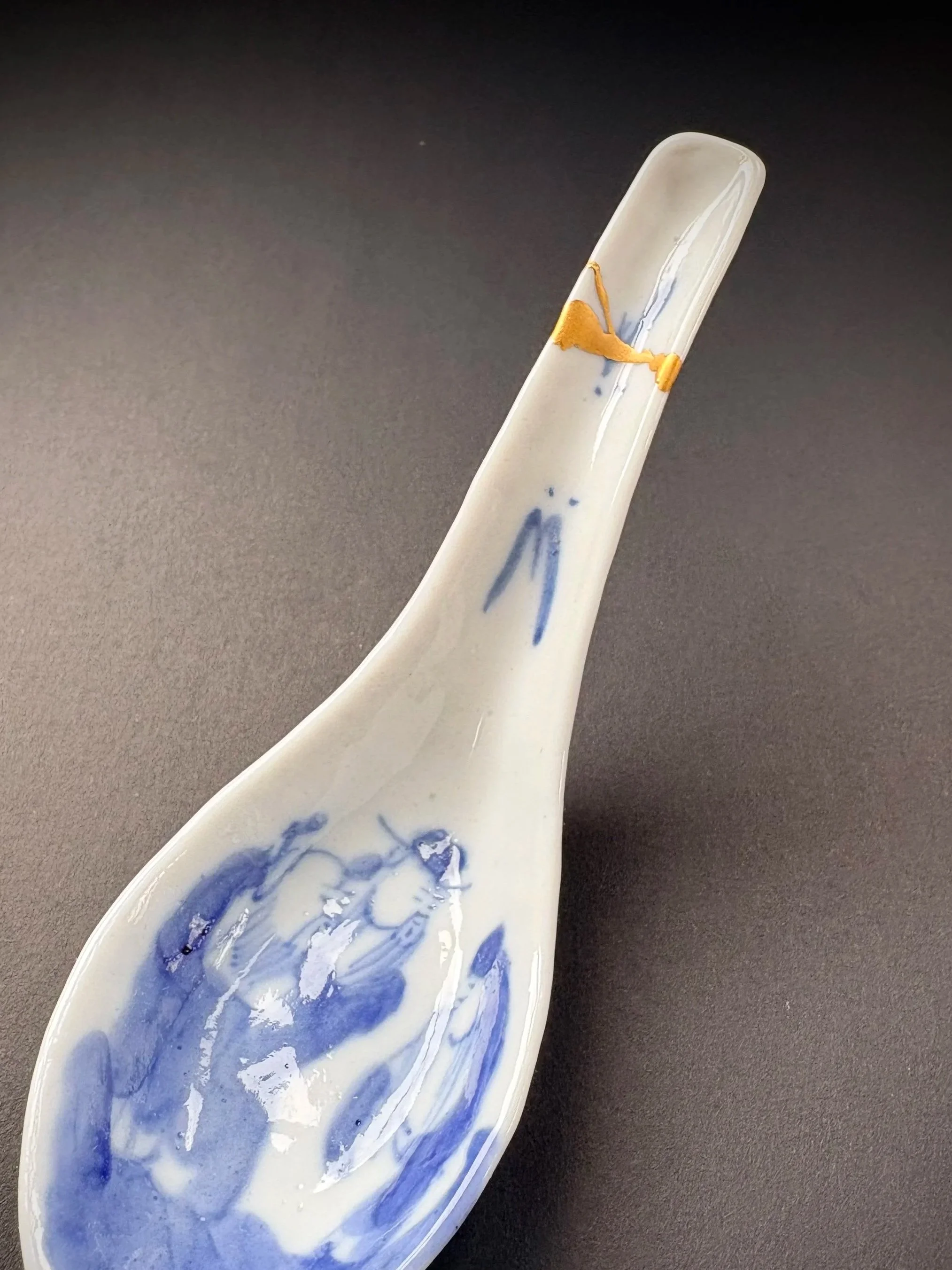 A white porcelain spoon with blue artistic designs, resting on a dark surface.