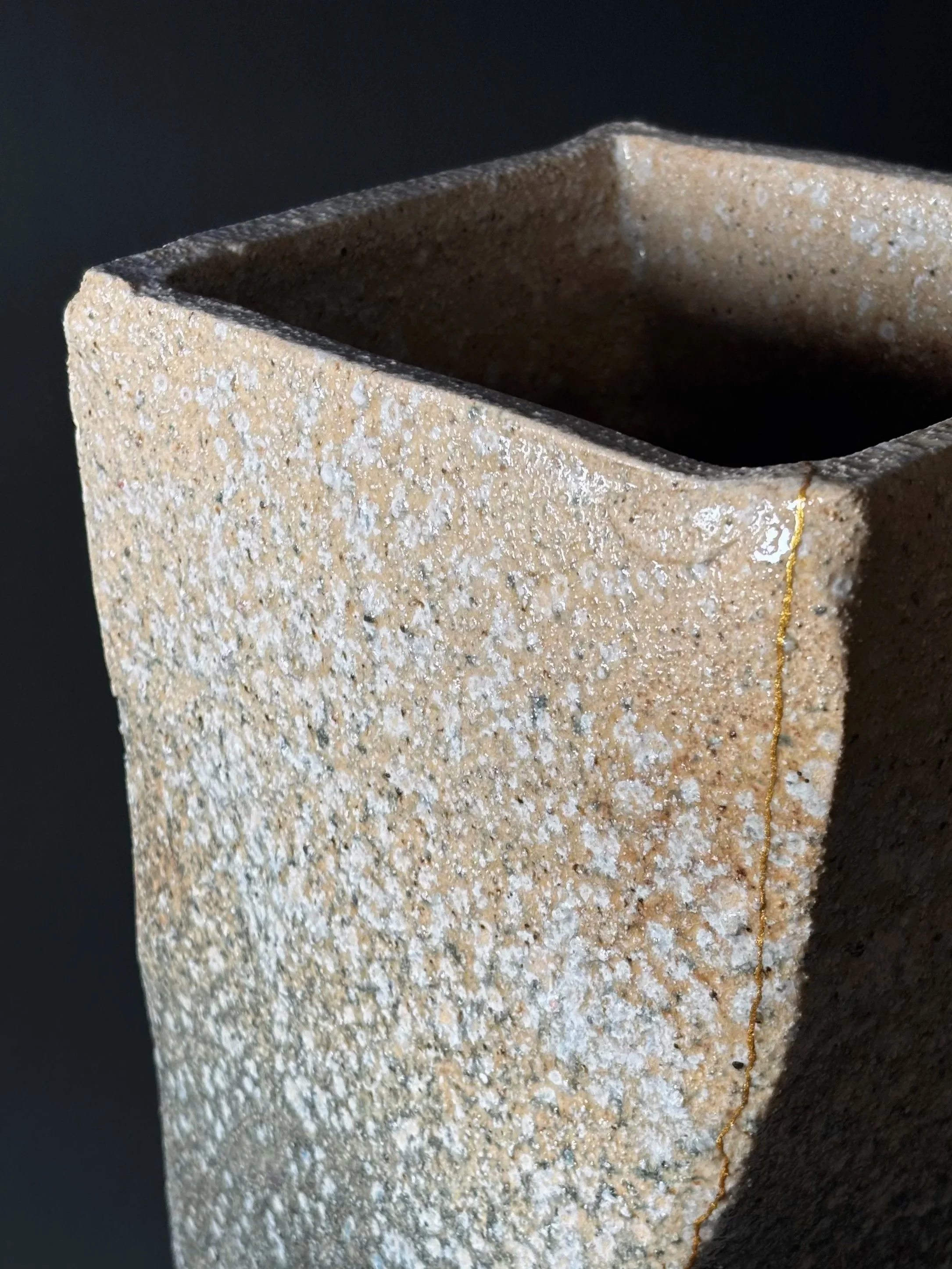 Close-up of a square-shaped, textured beige ceramic planter with a dark interior, set against a black background.