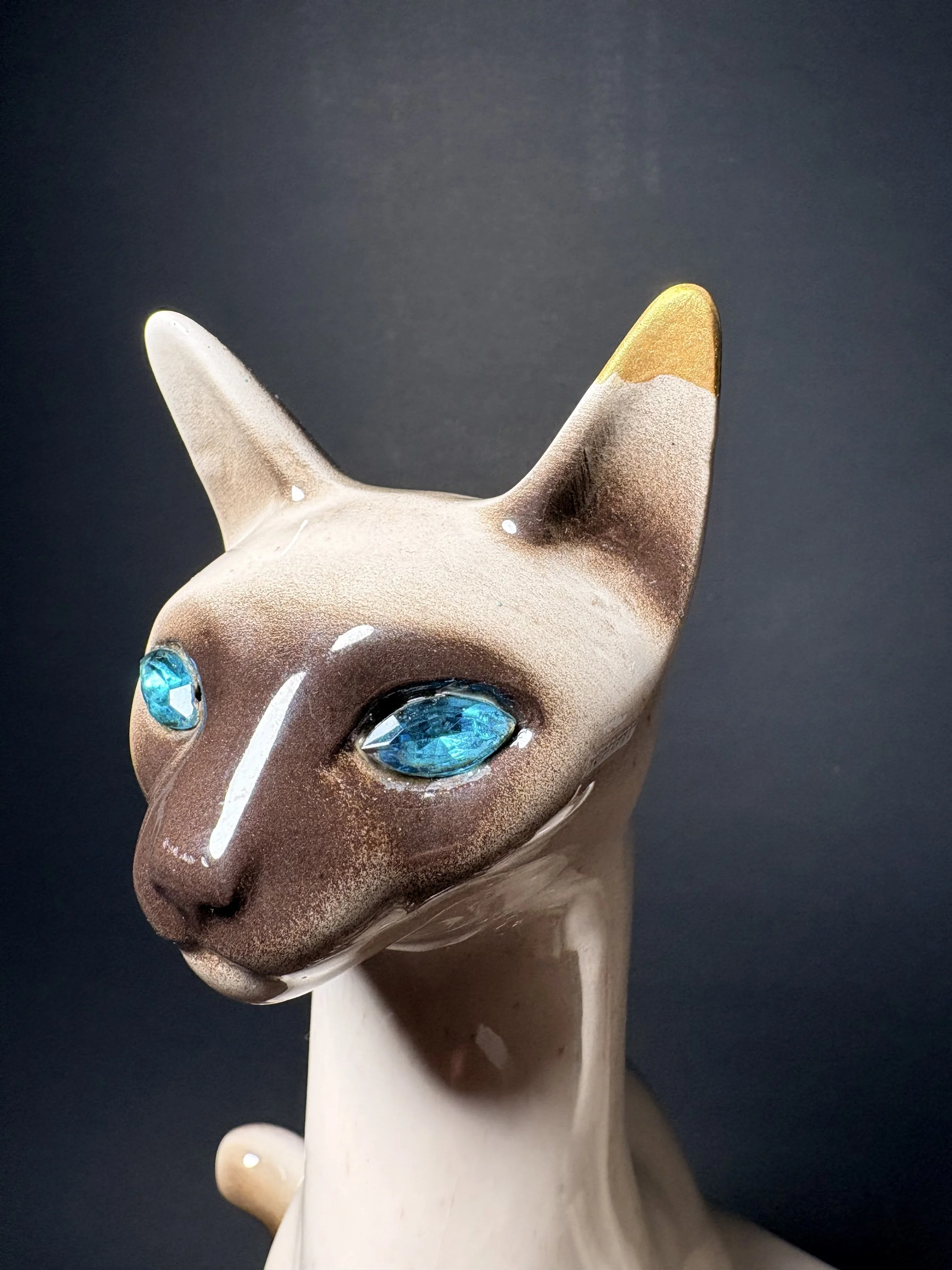 Close-up of a unicorn head figurine with blue gemstone eyes, a golden horn, and a pinkish-white mane, set against a dark background.