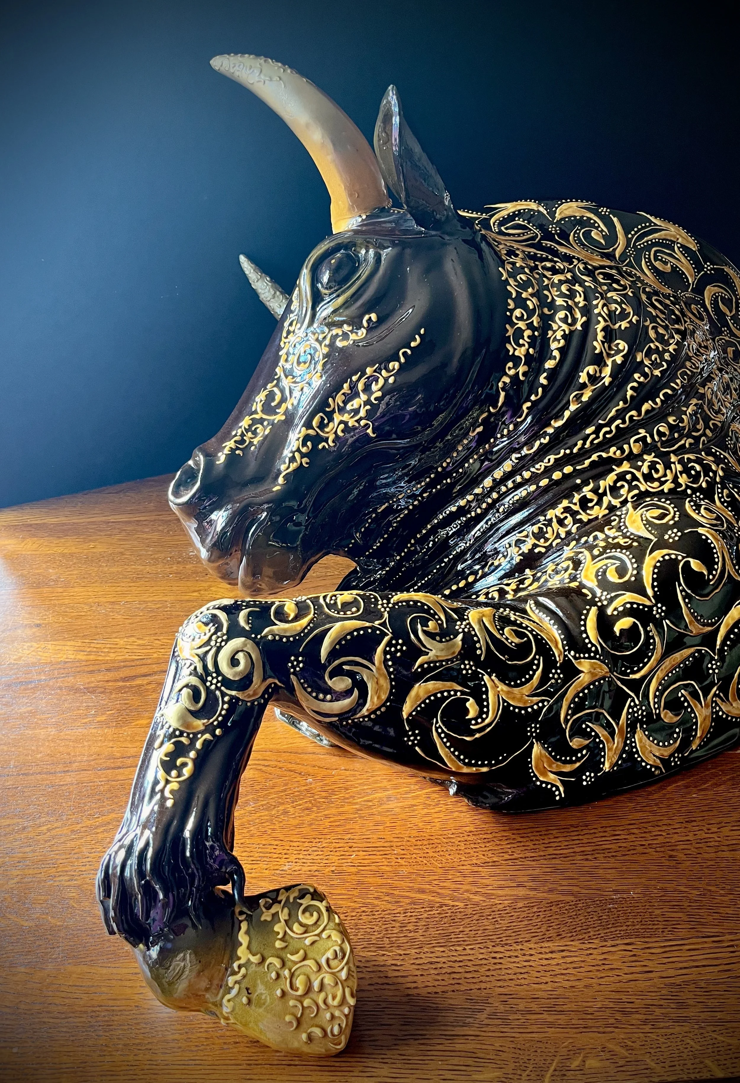 Decorative ceramic sculpture of a unicorn with black and gold ornate patterns, positioned on a wooden surface against a dark background.