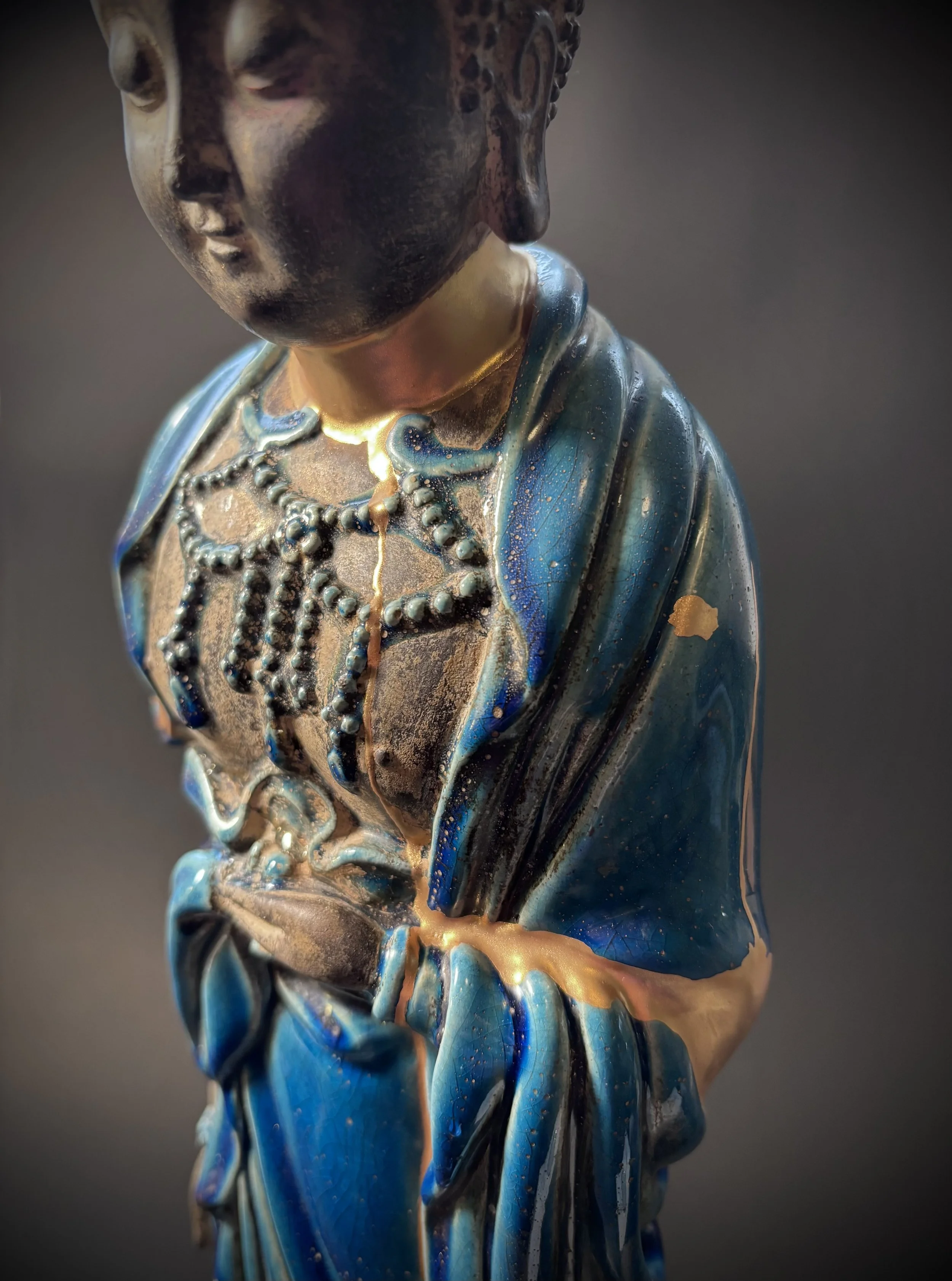 Close-up of a decorative glass sculpture of a woman wearing a necklace and a blue garment, with intricate detailing and a glossy finish.