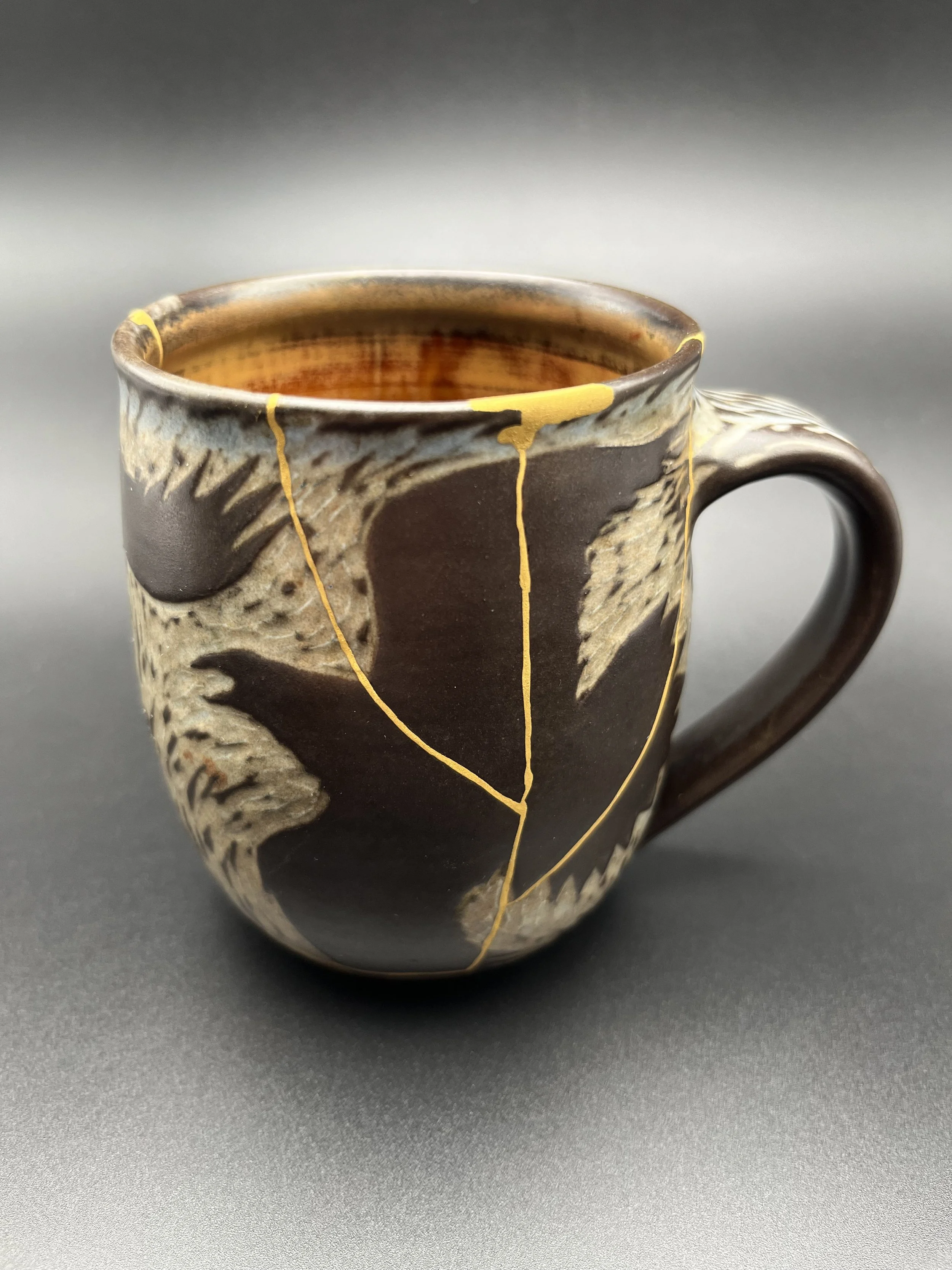 Close-up of a ceramic mug with dark brown and beige swirling patterns and yellow accents, filled with a dark liquid, with a plain gray background.