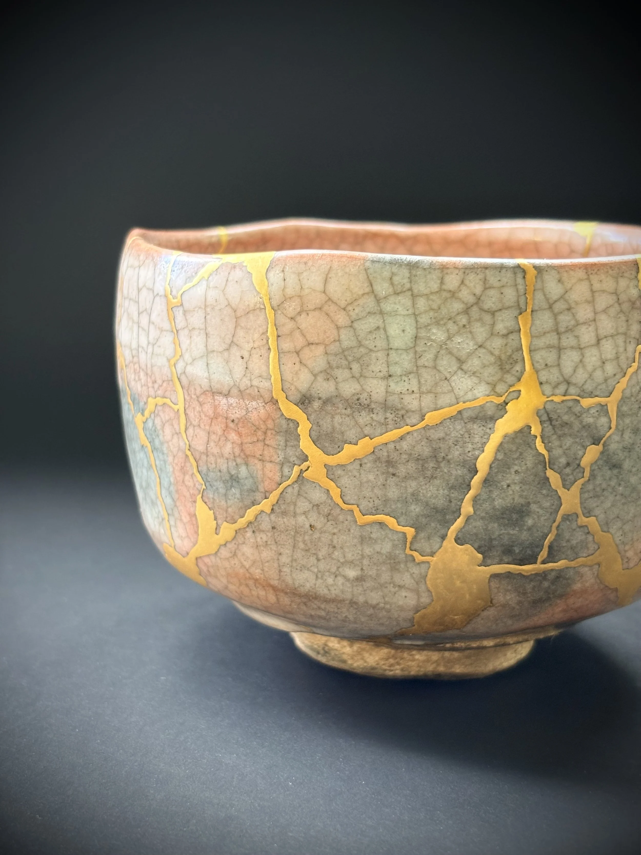 Close-up of a ceramic bowl with a crackled glaze pattern featuring pink, beige, and yellow hues, against a dark background.