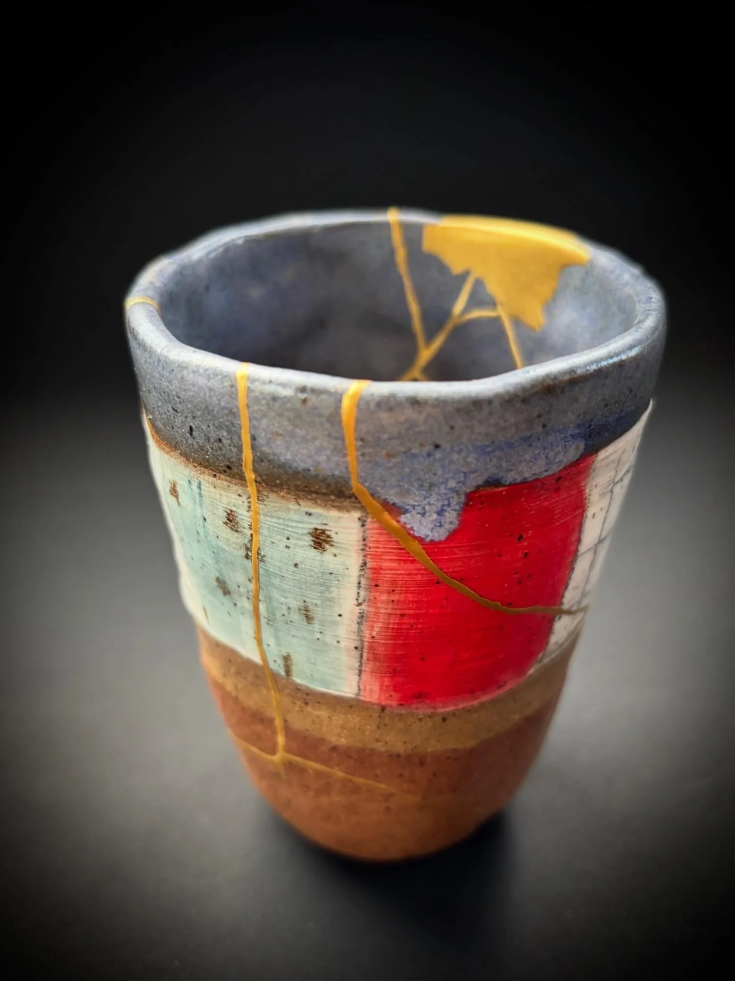 Close-up of a multicolored ceramic cup with a black background, showing a glossy glaze and cracks with gold accents.