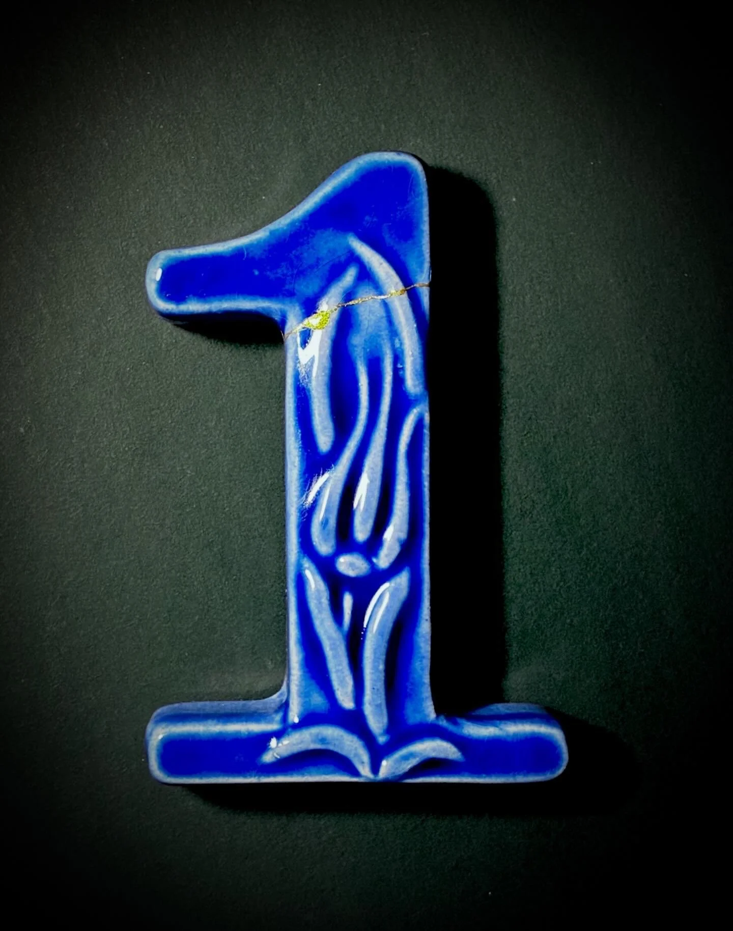 A blue glass sculpture resembling an abstract human figure standing against a black background.