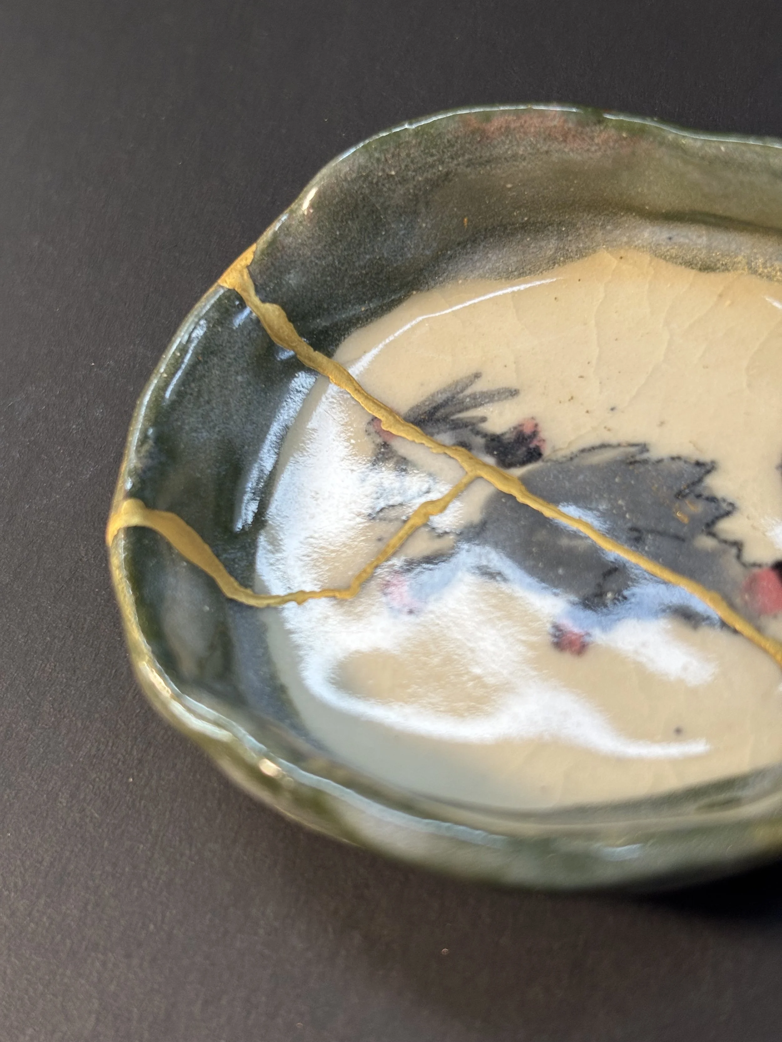 Close-up of a decorative ceramic bowl with a floral design and gold rim, placed on a dark surface.