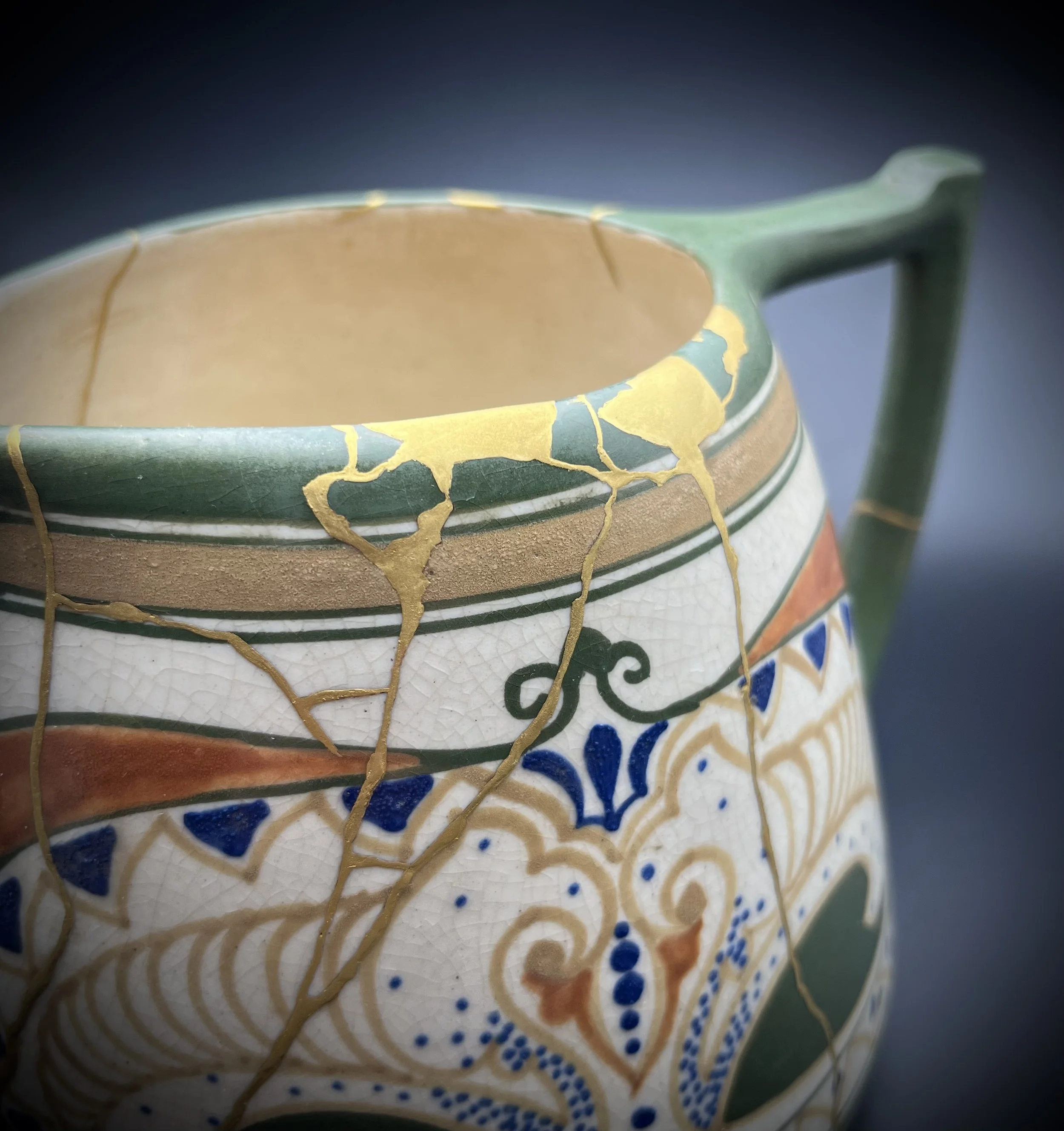 Close-up of a colorful ceramic mug with a cracked glaze finish, featuring decorative patterns in gold, green, orange, blue, and white.