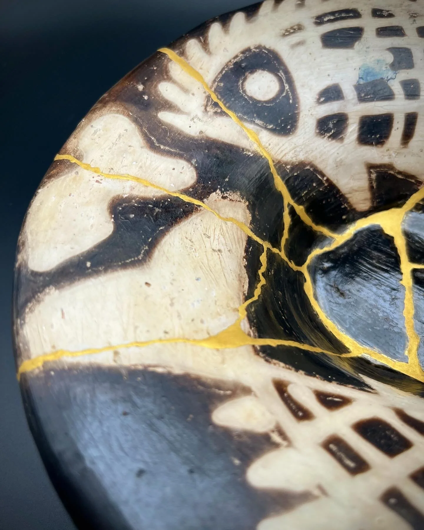 Close-up of a carved wooden mask with black, white, and yellow painted patterns and cracks in the wood.