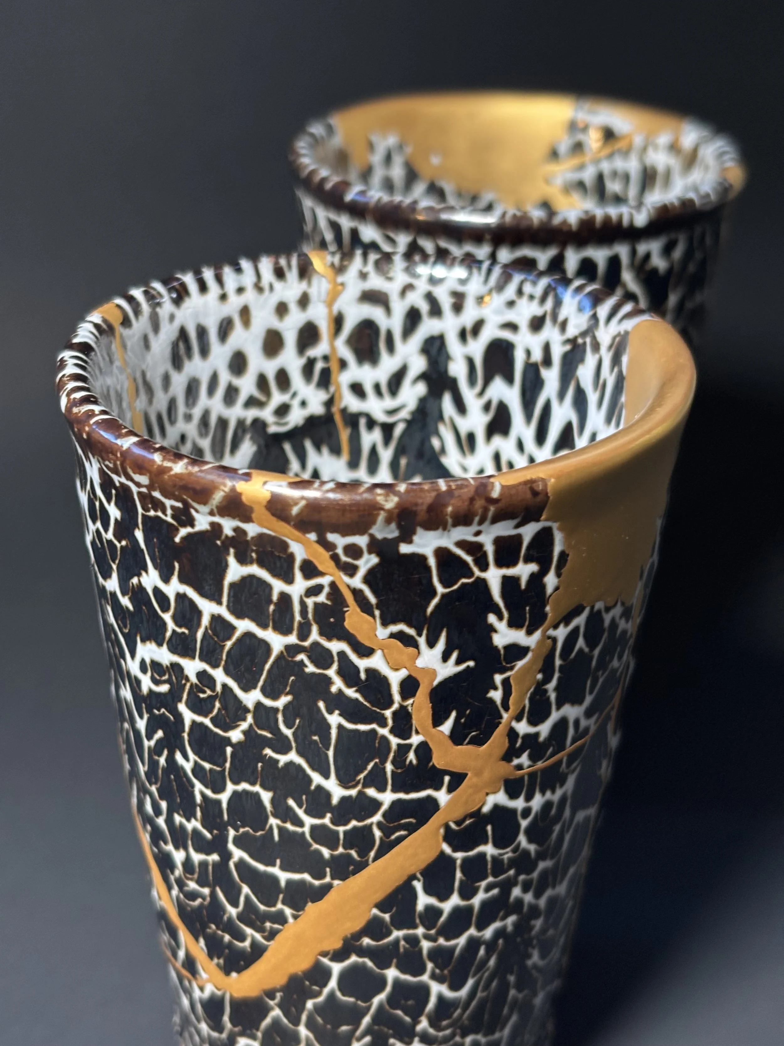 A decorative ceramic cup with a black and white cracked pattern and brown accents, placed against a dark background.