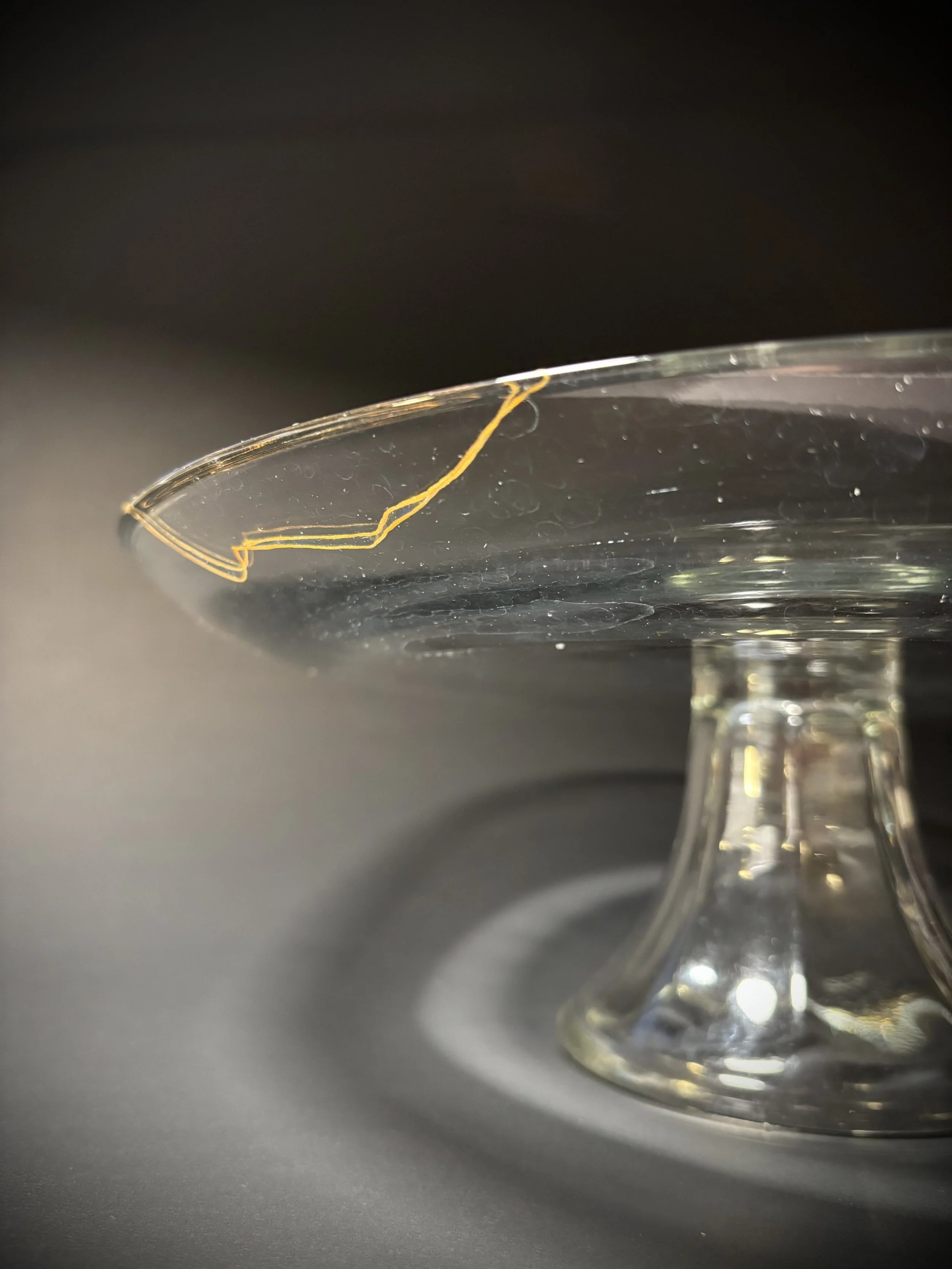 Close-up of a glass bowl with a small crack on the rim, sitting on a dark surface with a plain dark background.