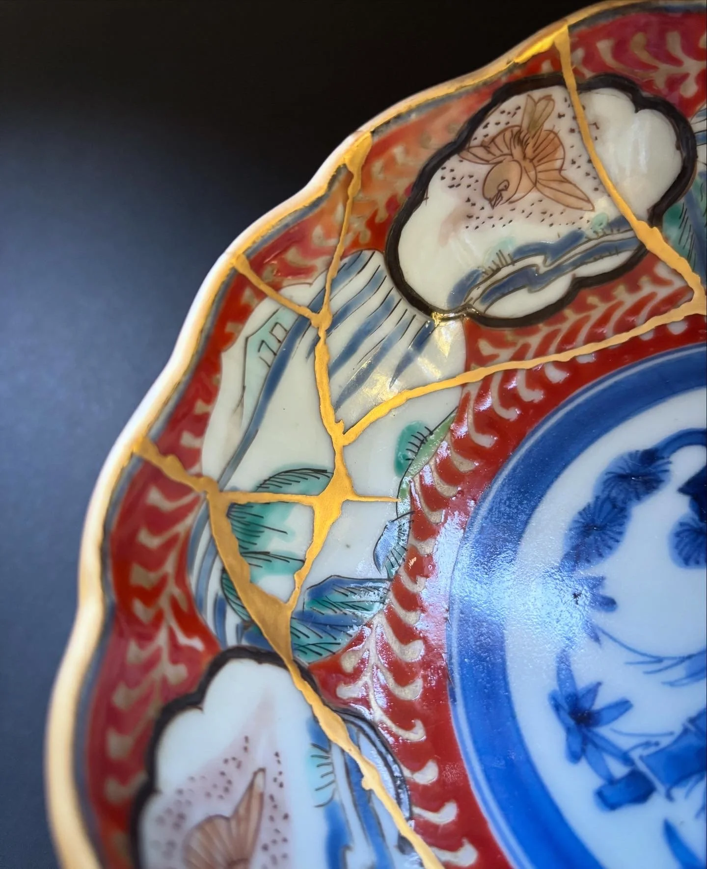 Close-up of a colorful, decorated ceramic or porcelain plate with ornate patterns, including a flower and abstract designs, featuring vibrant colors like red, blue, white, and gold accents.