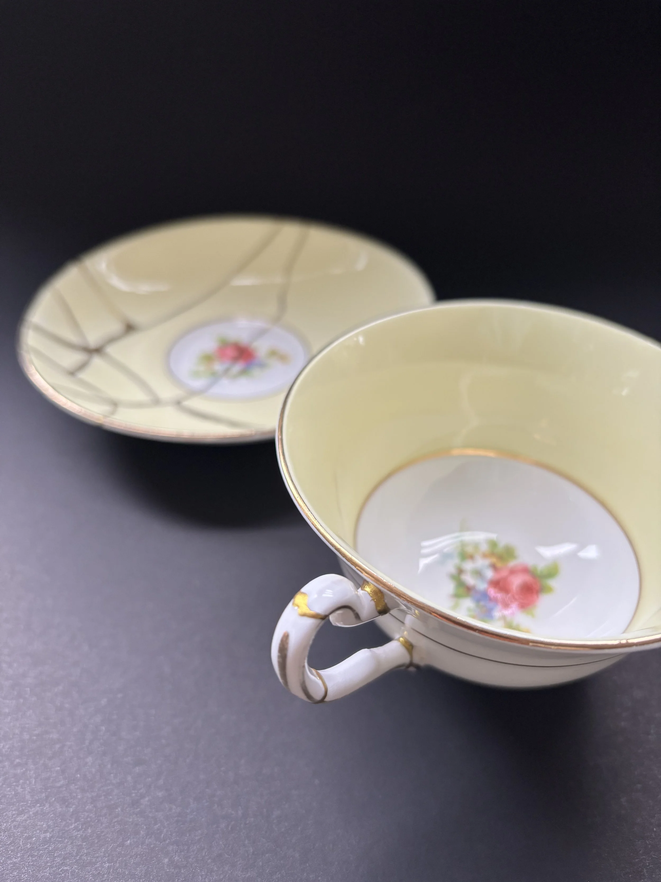 A porcelain teacup with a floral pattern, gold accents, and a decorative handle, placed on a dark surface.
