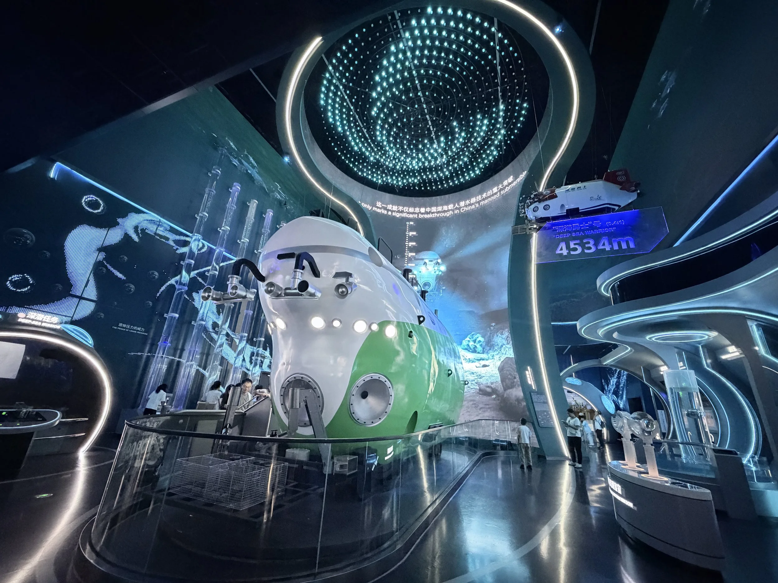 Indoor exhibit featuring a model of a spacecraft, digital displays, and a large illuminated digital globe or nebula overhead at a Shenzhen science or technology museum.