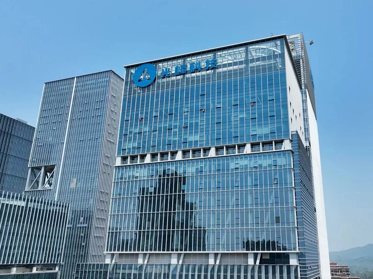 A modern glass office building with blue signage on top, set against a clear blue sky.