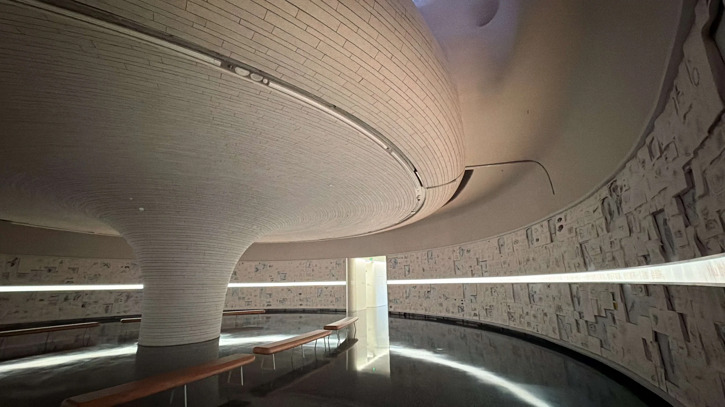 Shenzhen Cultural Square signage design: Wayfinding in modern interior with curved ceiling, brick wall, and benches.