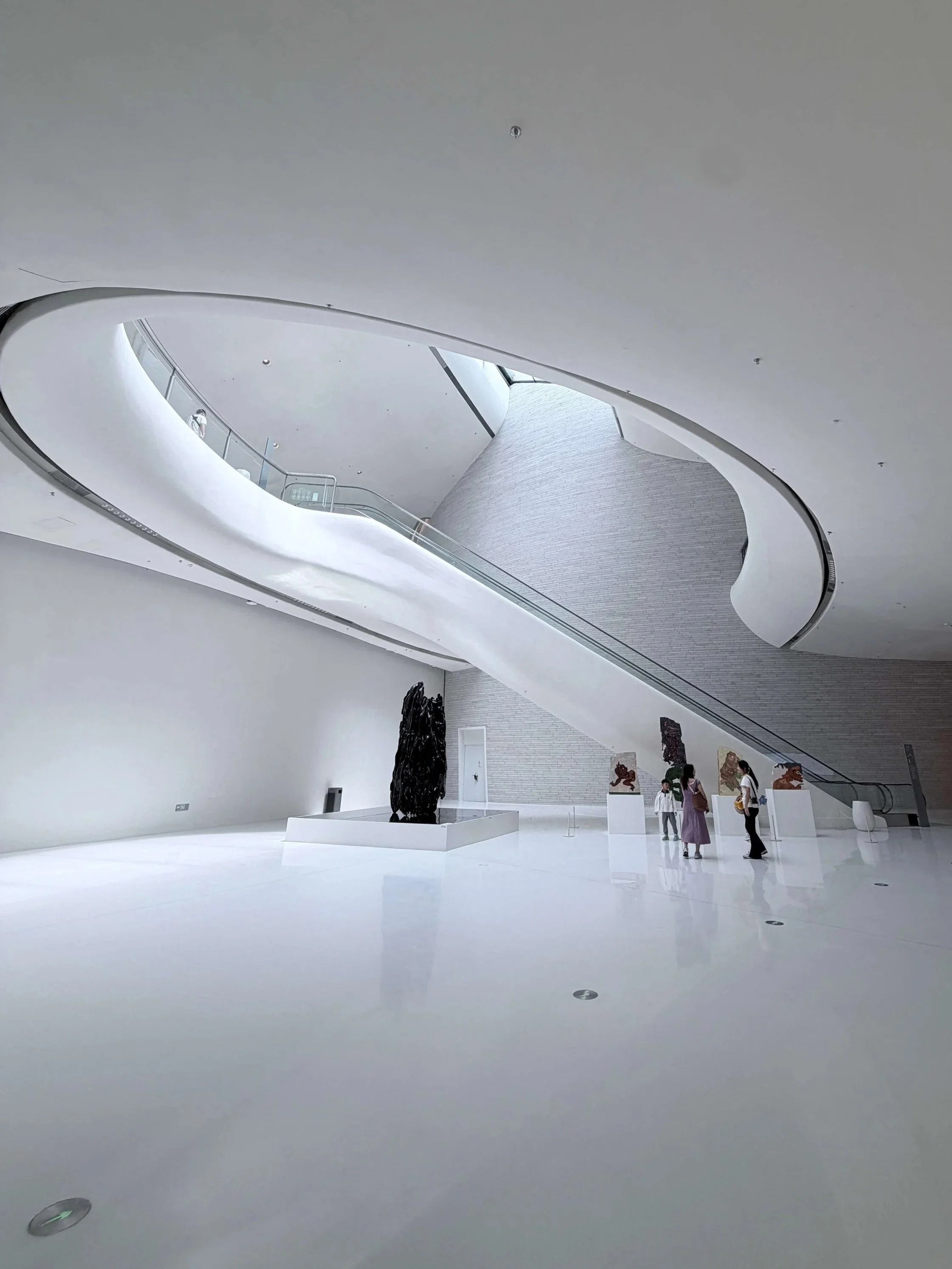 Shenzhen Cultural Square interior: Visitors viewing sculptures on pedestals inside minimalist curved white gall