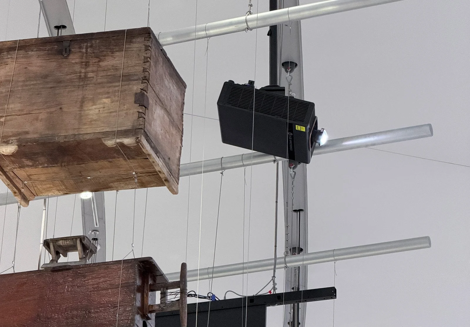Ceiling with suspended wooden crates and metal beams, a black speaker or projector attached to a metal structure, and wires running along the ceiling.