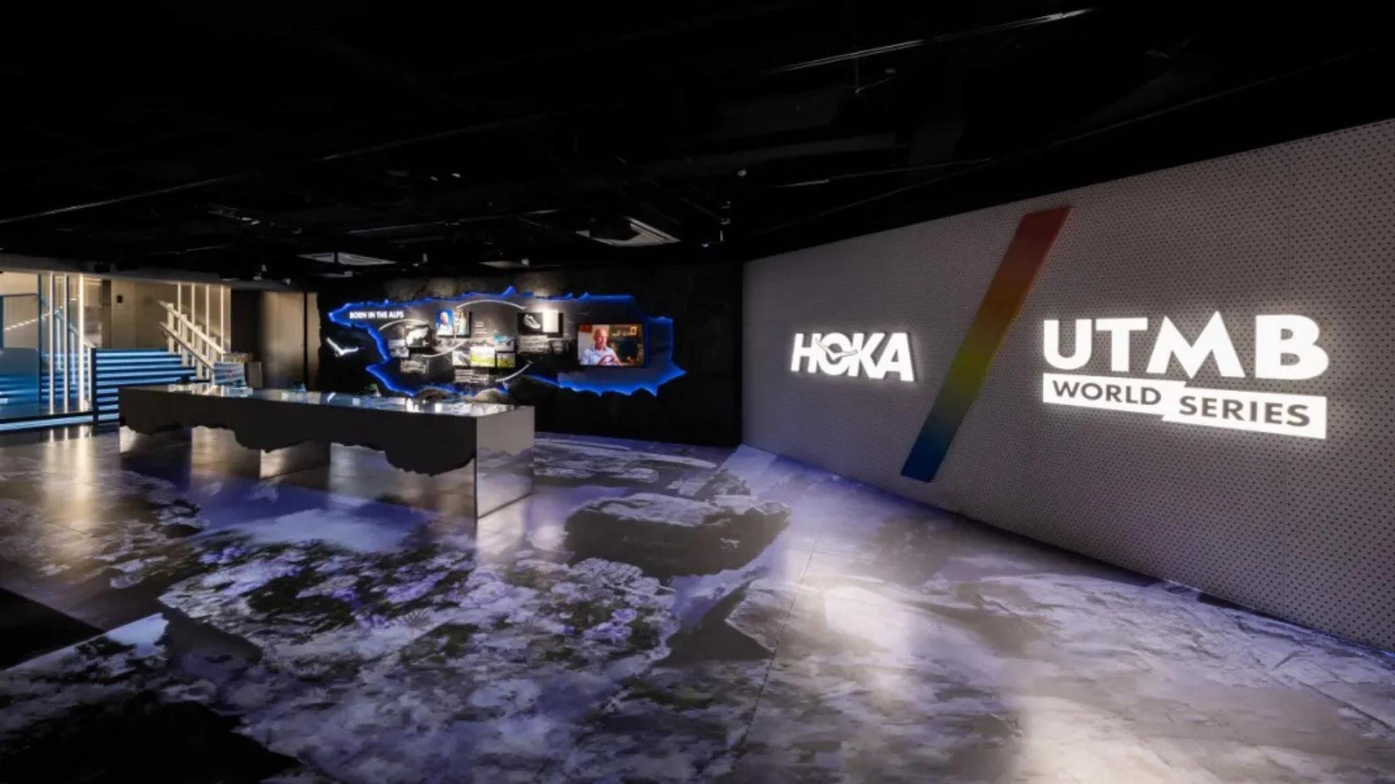 HOKA Experience Center: Modern space with digital screens displaying HOKA and UTMB logos and interactive video call.
