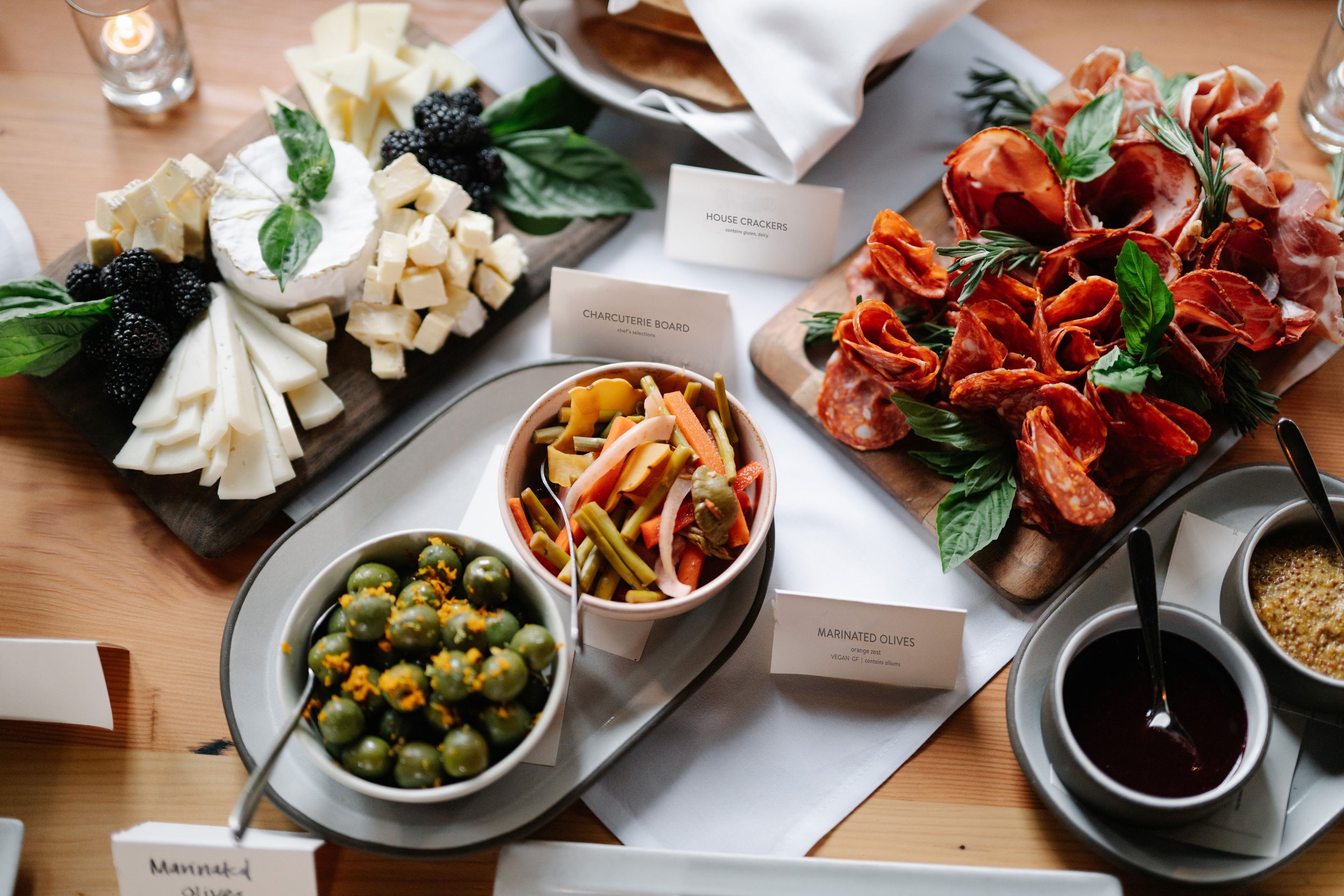 A variety of appetizers on display, including cheese and blackberries, charcuterie, marinated olives, pickled vegetables, and dipping sauces.