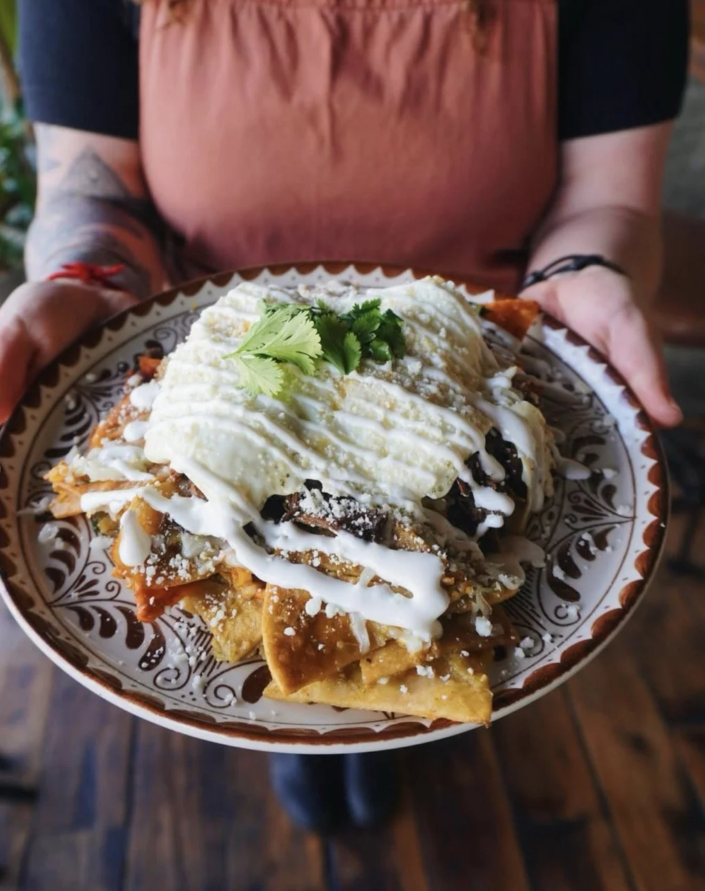 Person holding a bowl of loaded nachos topped with sour cream and cilantro garnishes.
