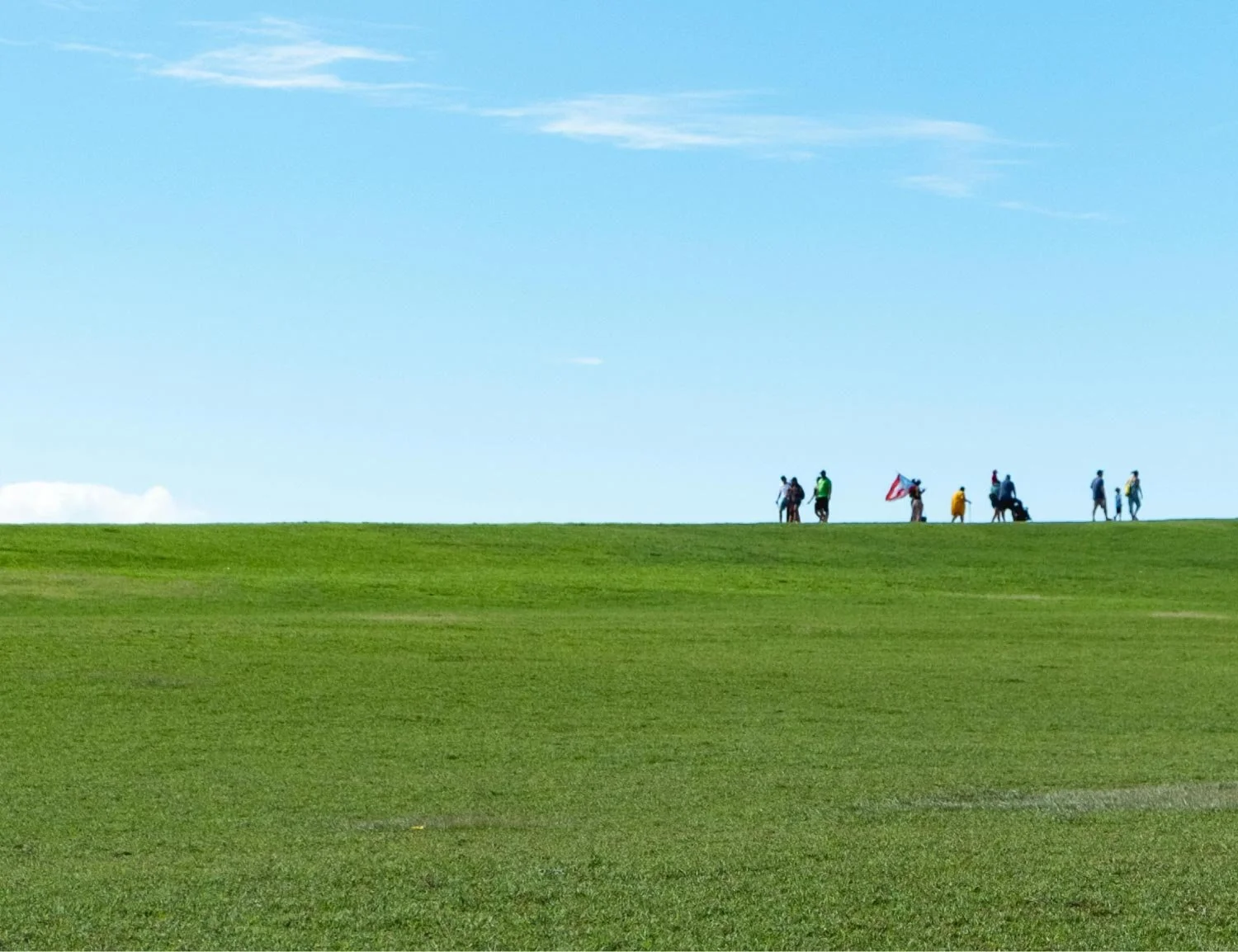 People walking on a grassy hilltop under a clear blue sky.