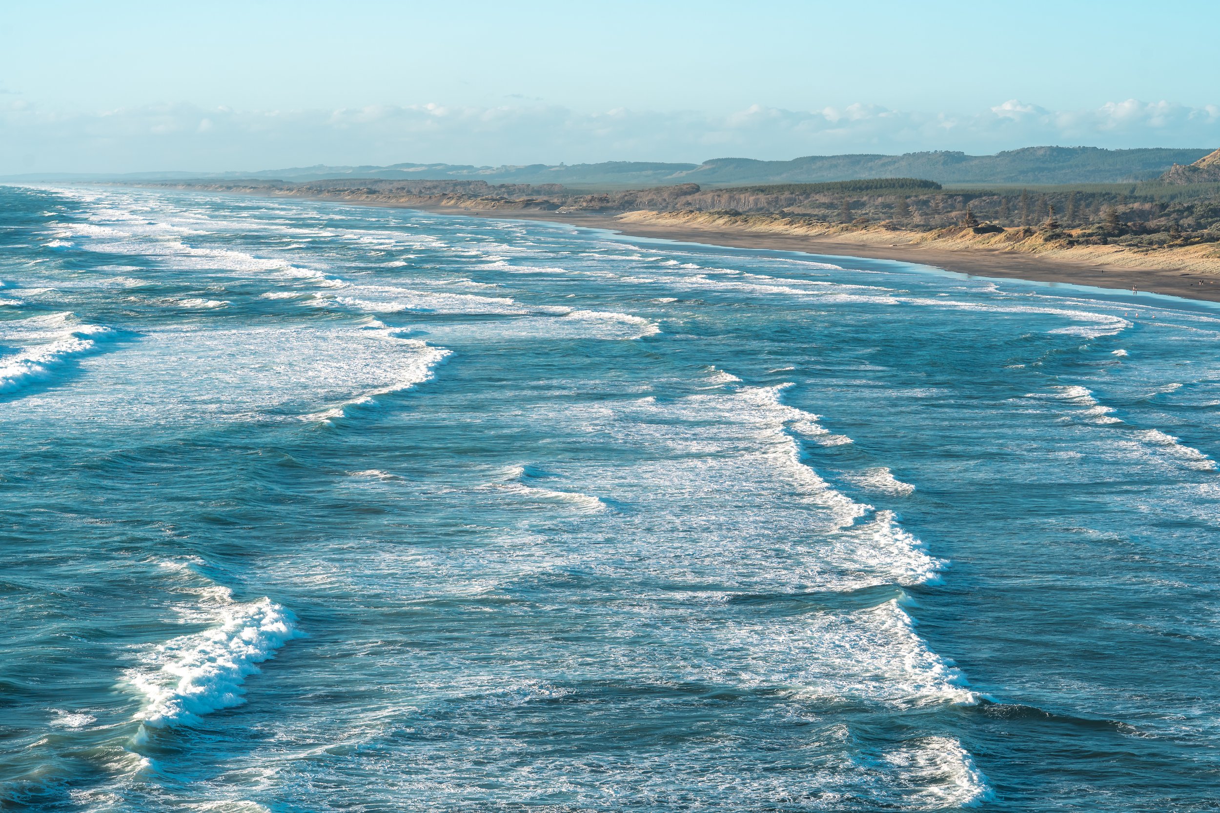 A view of the ocean with waves and a distant shoreline under a partly cloudy sky.
