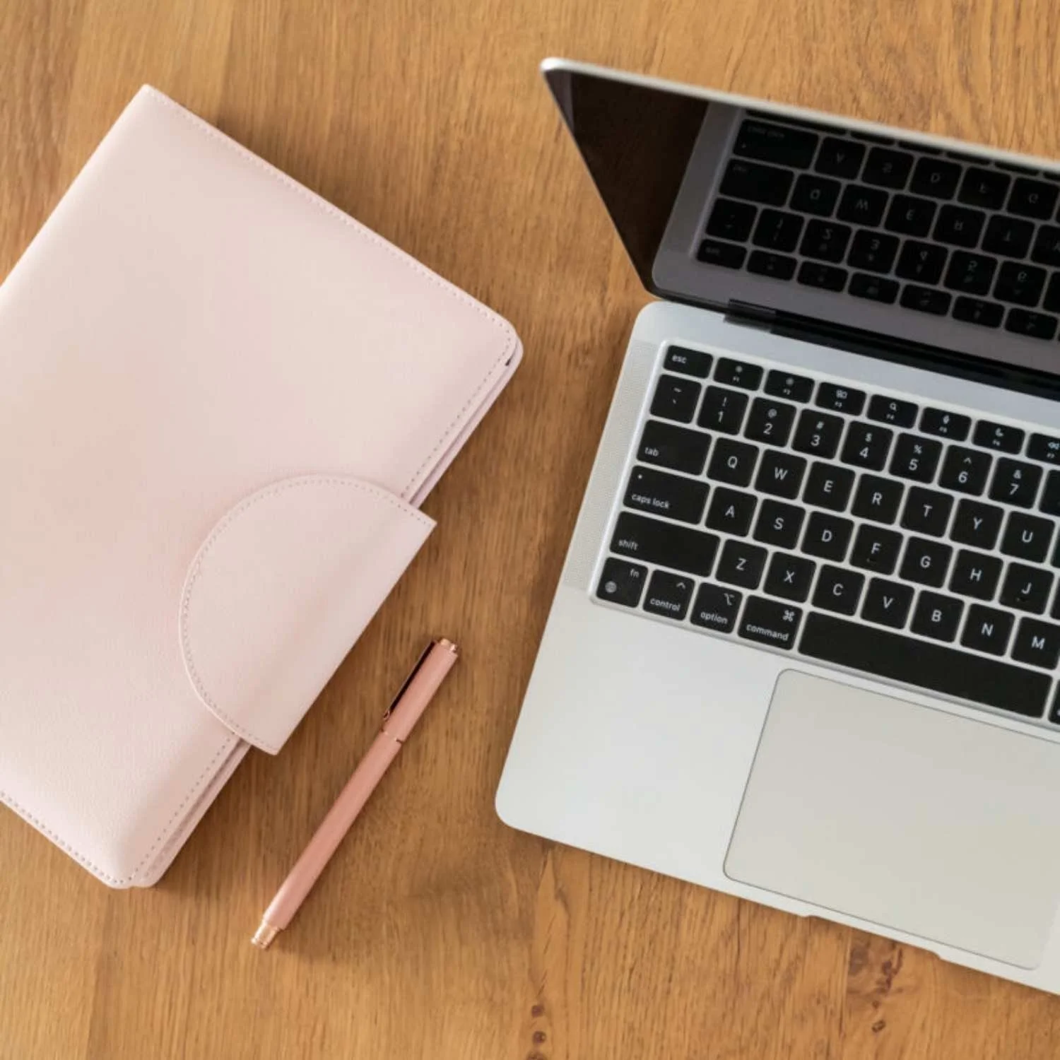 Laptop, pink planner and pen on a wooden desk for career consulting and planning.