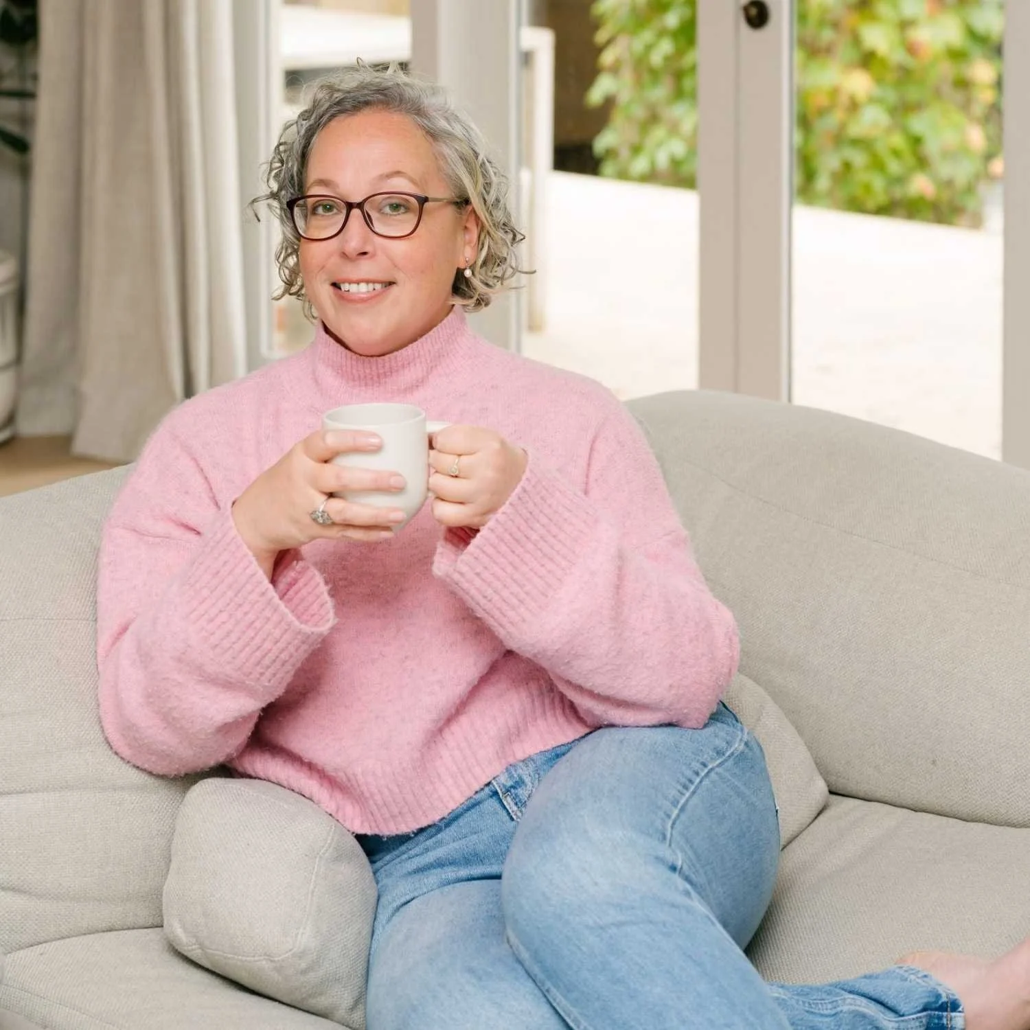 Hannah from Small Circle, a career coach and strategist, holding a coffee on a couch in a relaxed professional setting.