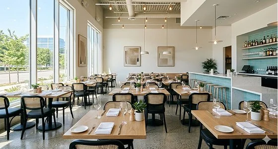 A pristine, spotlessly clean modern restaurant dining room featuring immaculate wooden tables, dust-free woven back chairs, sparkling glassware, and a flawless polished concrete floor.