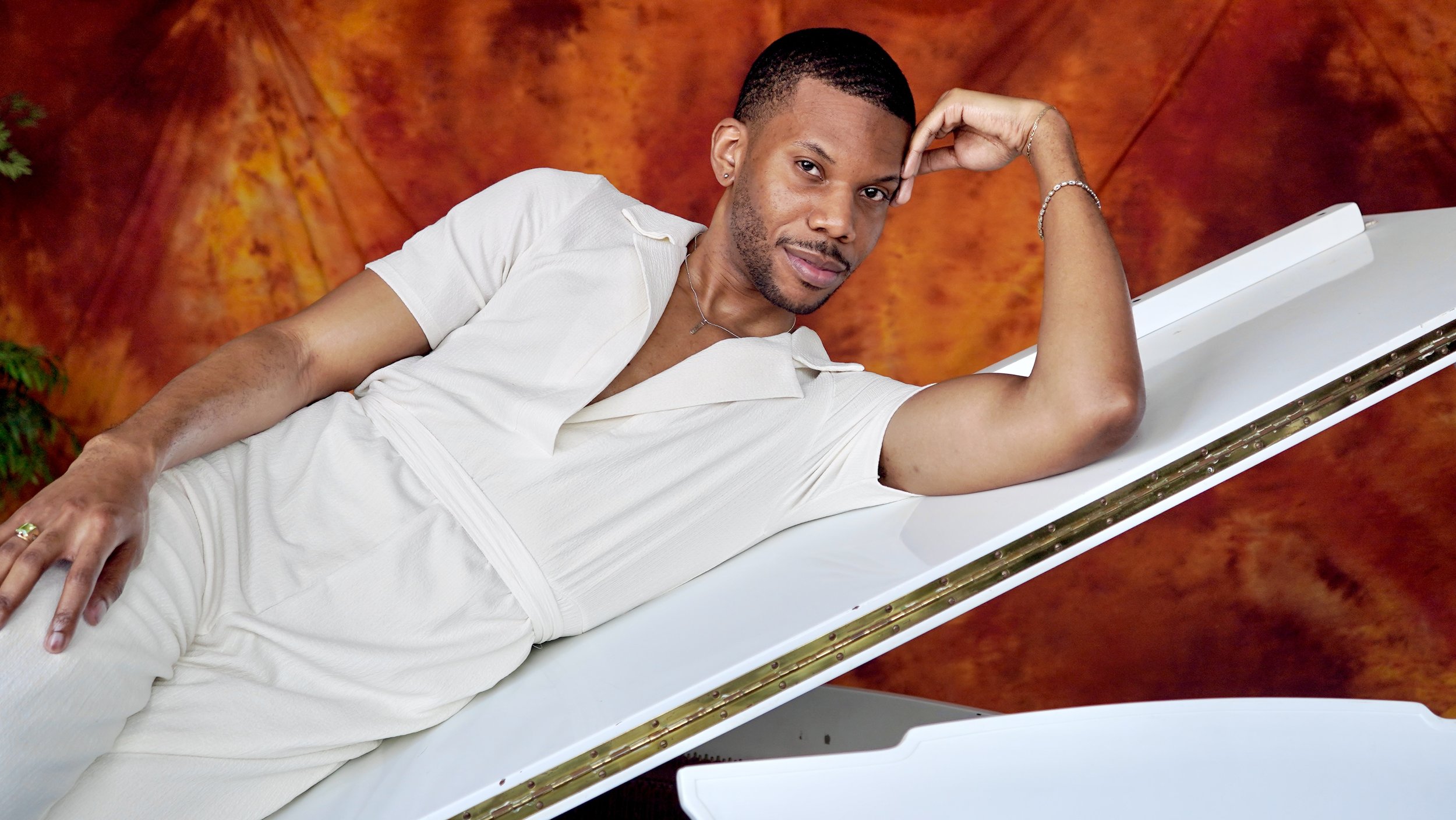Aaron-Casey lying on a white grand piano, with a warm orange and brown background.