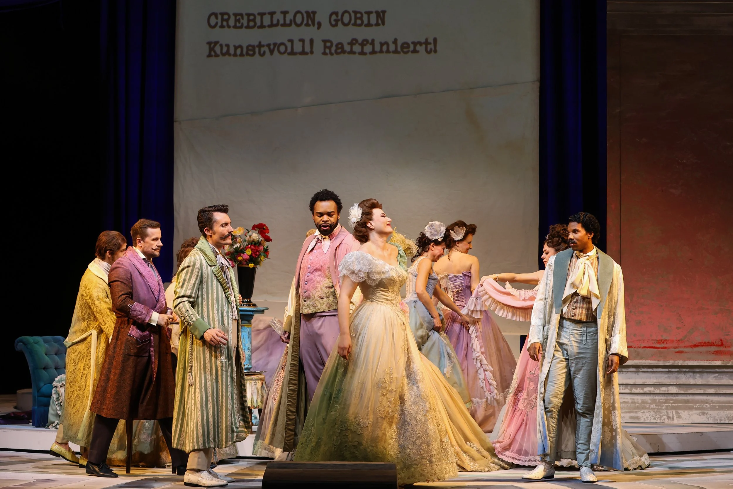 Actors dressed in historical costumes on stage, performing a scene in a theater production.