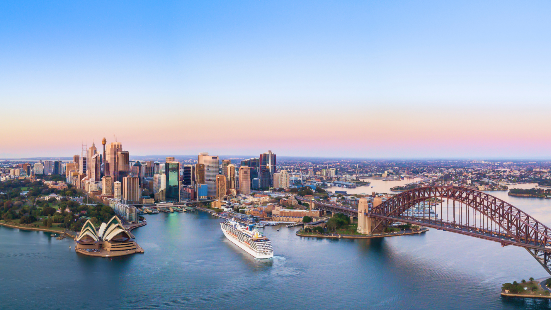 Aerial view of Sydney skyline at sunset, featuring the Sydney Opera House, Harbour Bridge, and a cruise ship in the harbor.