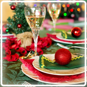 Festive table setting with green and red decor, sparkling wine glasses, Christmas ornaments, and a small tree, creating a joyful mood.