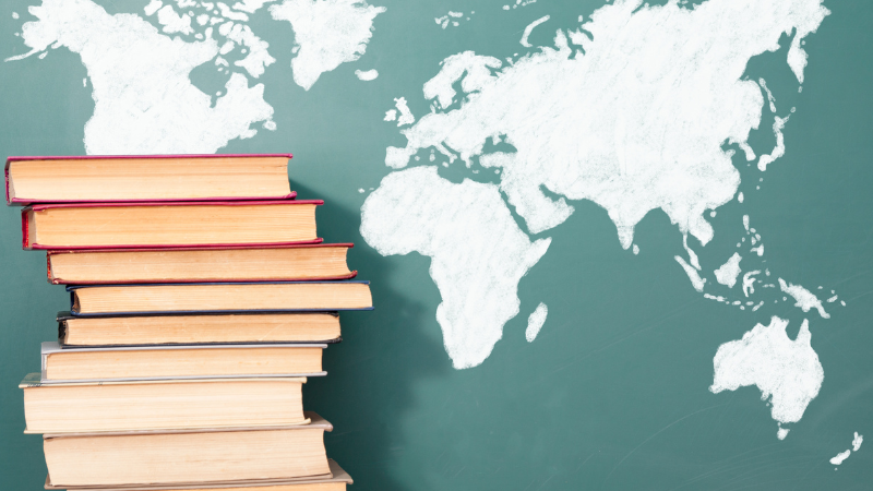 Stack of books next to a chalk-drawn world map on a green chalkboard. The image suggests learning and exploration.